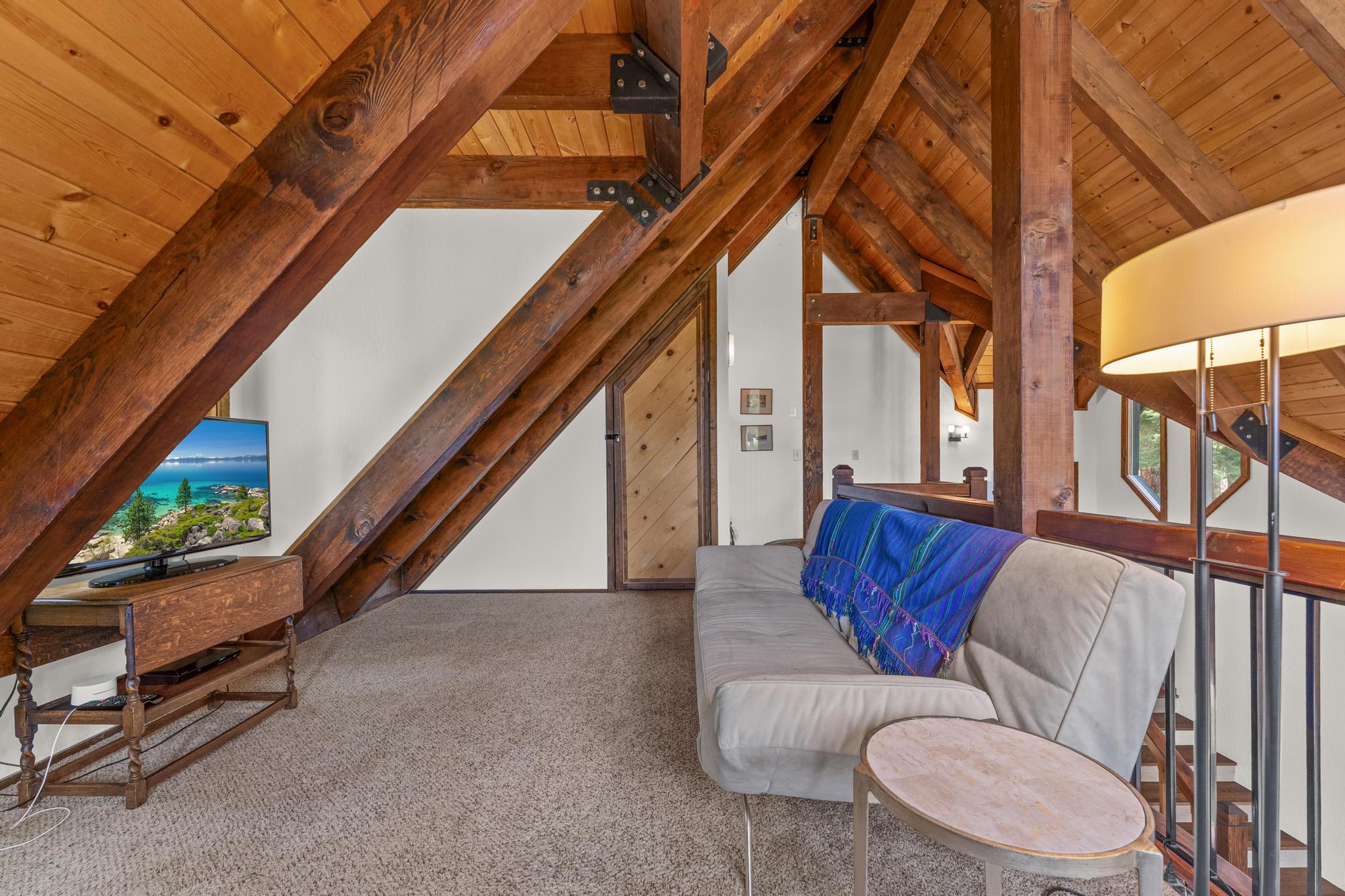 Cozy loft in a Tahoe Vista vacation rental with wooden beams, couch, TV, and mountain views for relaxation.