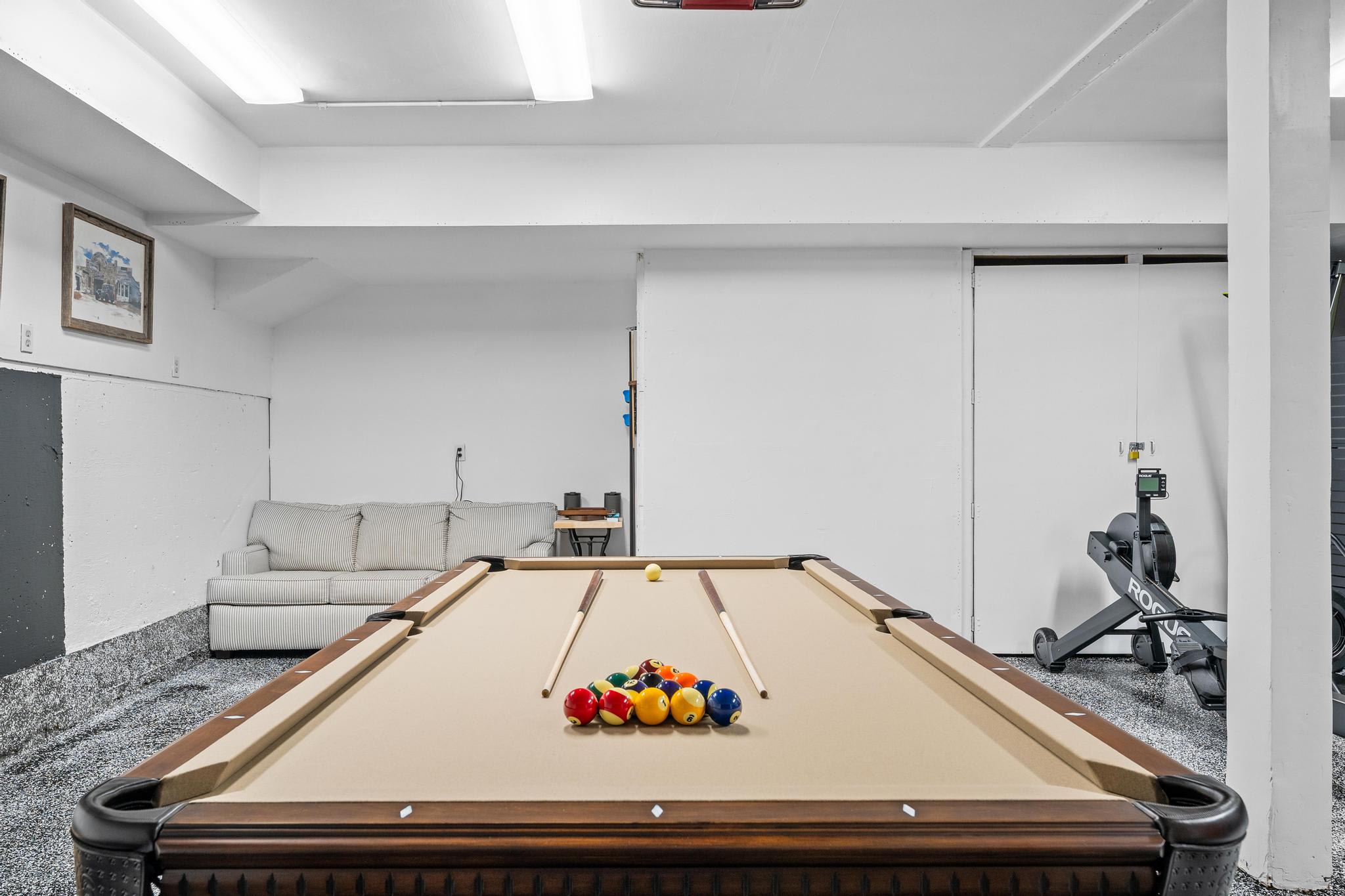 Pool table and couch in a Truckee vacation rental, featuring a rowing machine and wall art in a cozy game room.