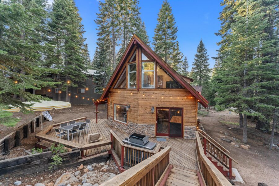 A charming Tahoe Vista vacation rental cabin with wood exterior, surrounded by pine trees, featuring a deck with seating.