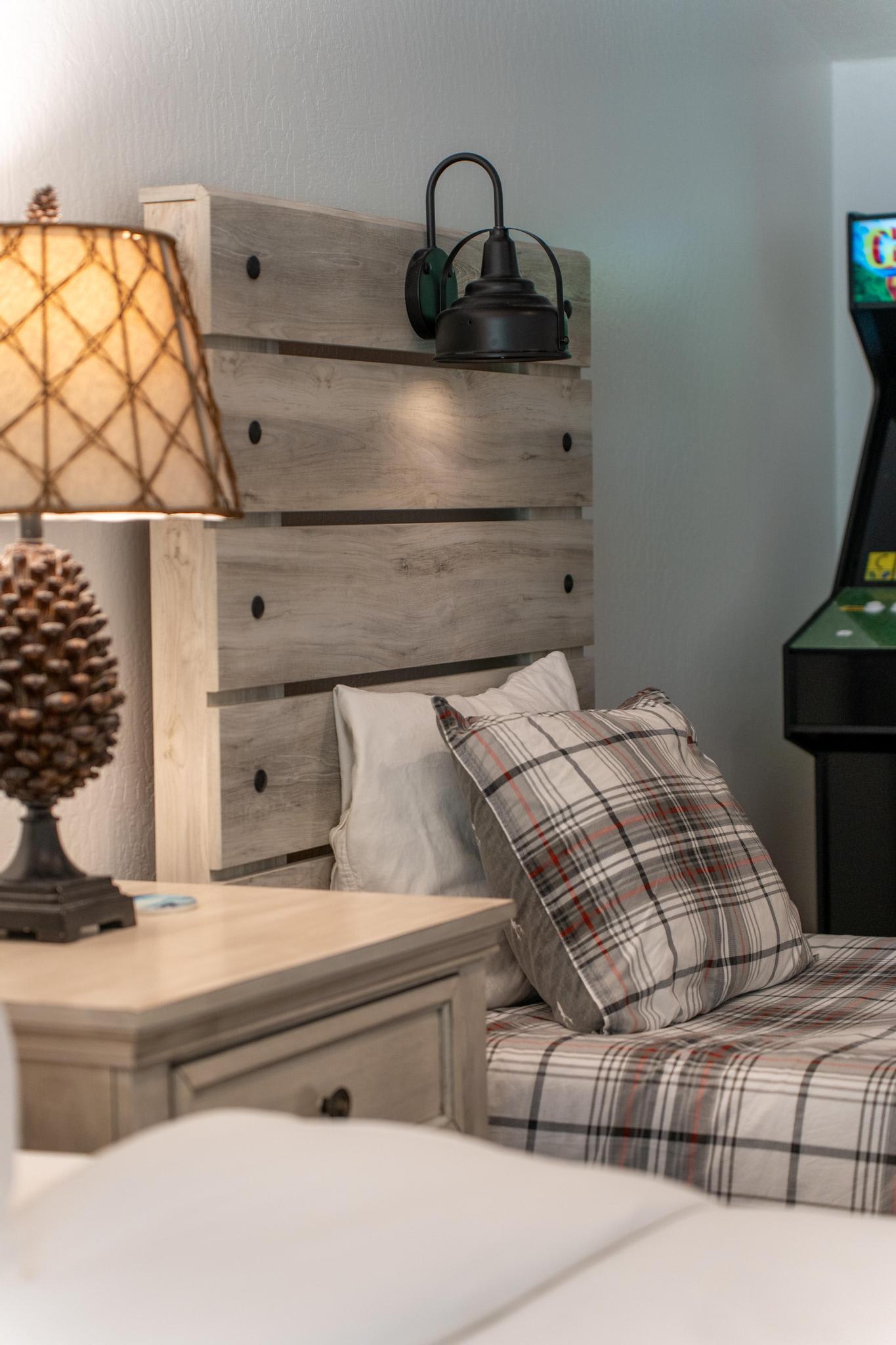 Cozy Truckee vacation rental bedroom with plaid bedding, rustic wood headboard, pinecone lamp, and an arcade game.
