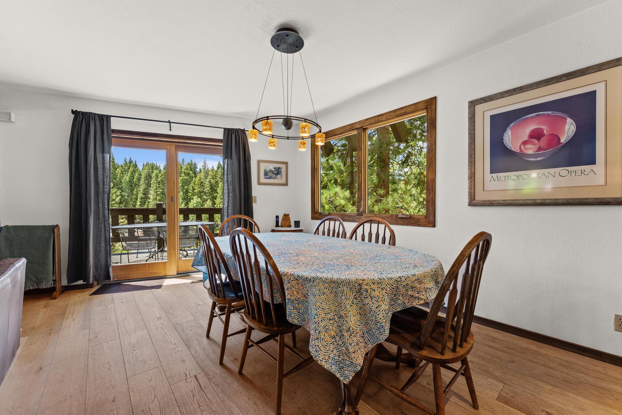 Dining area in a Tahoe Vista vacation rental with a table, wooden chairs, and forest view through large windows.