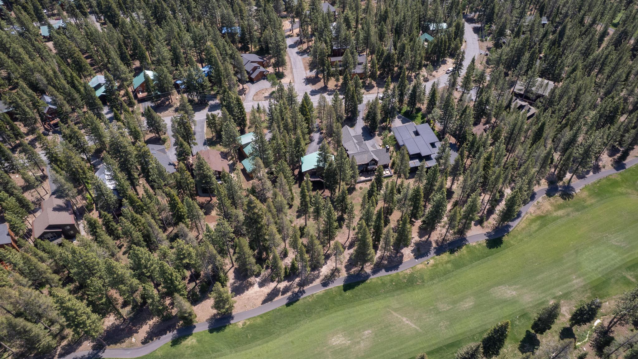 Aerial view of vacation rentals nestled in a forest near Truckee, with a winding path beside a green open area.