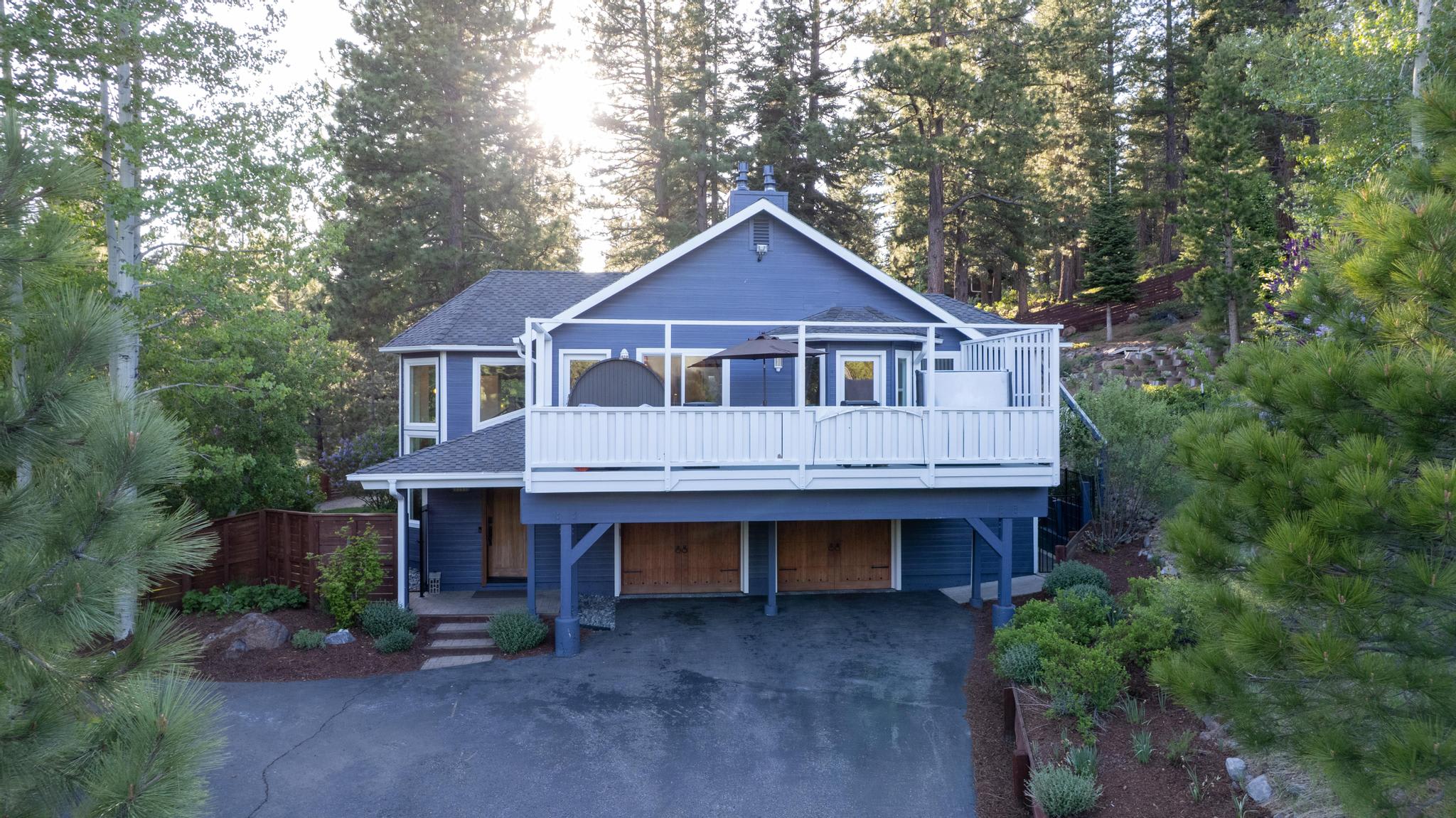 Charming blue vacation rental in Truckee, surrounded by pine trees, with a wraparound balcony and spacious driveway.