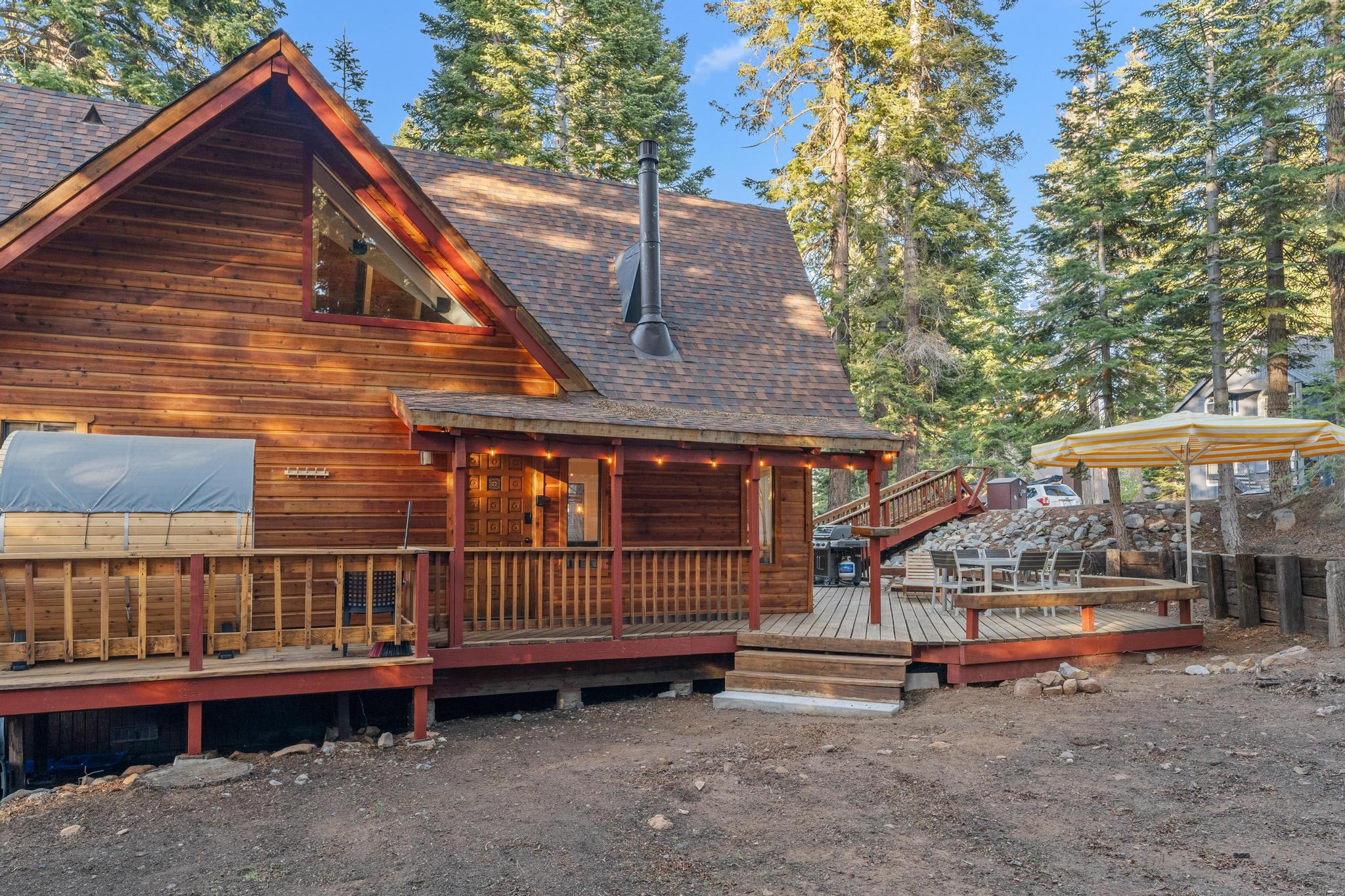 Rustic cabin vacation rental in Tahoe Vista with wooden deck, surrounded by tall pine trees and outdoor seating area.