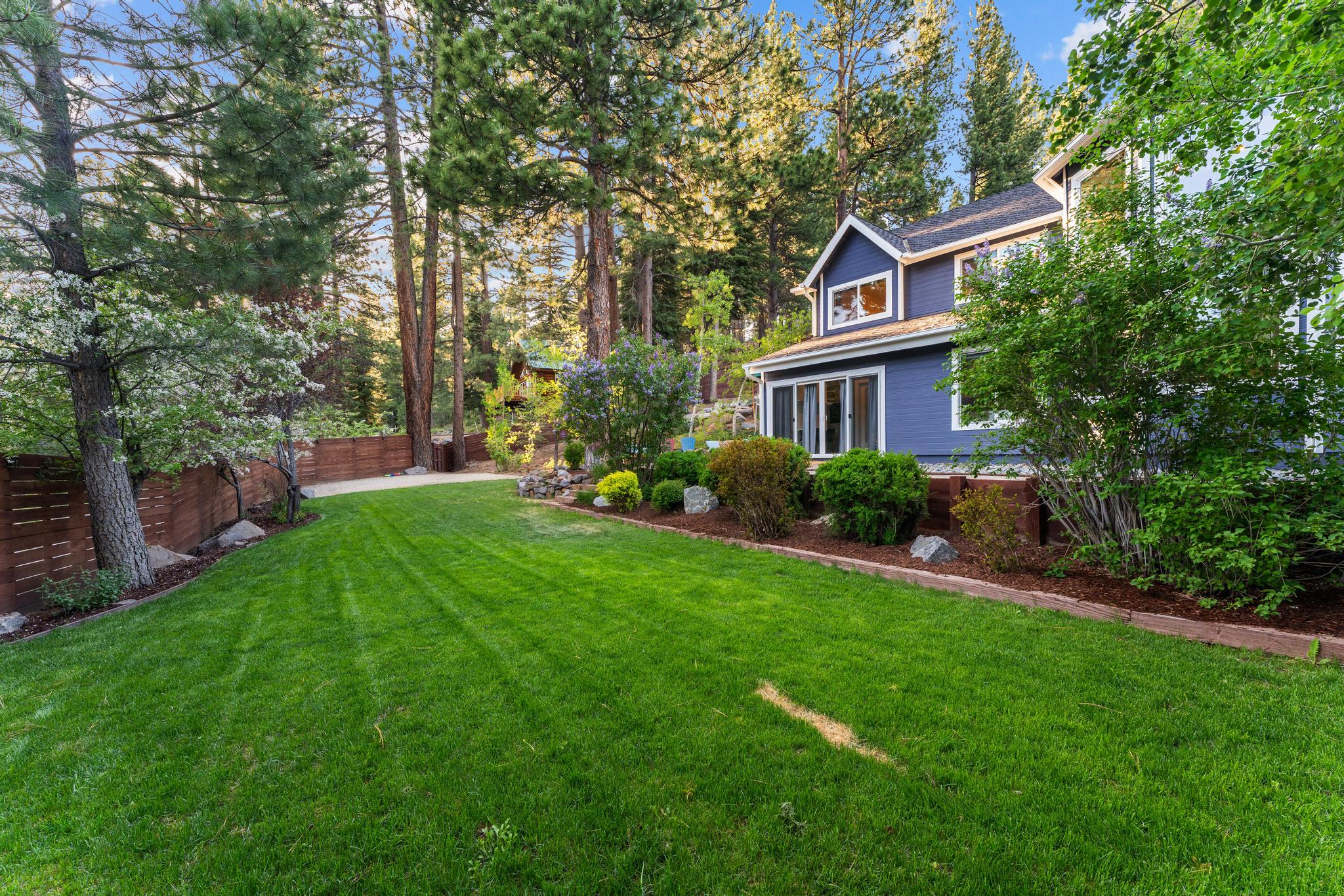 Vacation rental in Truckee with lush green lawn, surrounded by trees and shrubs, and a wooden fenced yard.