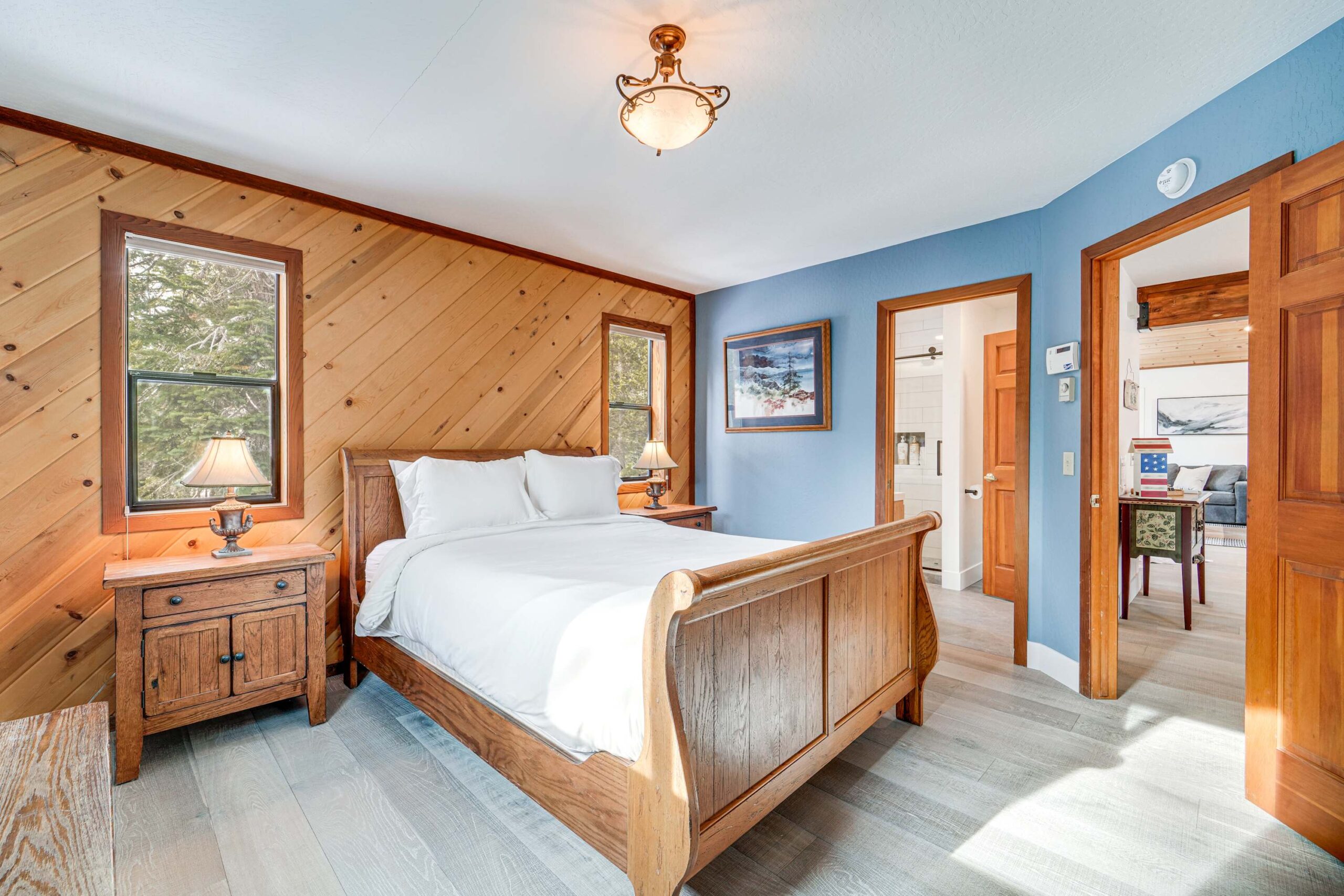 Cozy bedroom in Truckee vacation rental with wood panel walls, blue accents, stylish bed, and forest views.