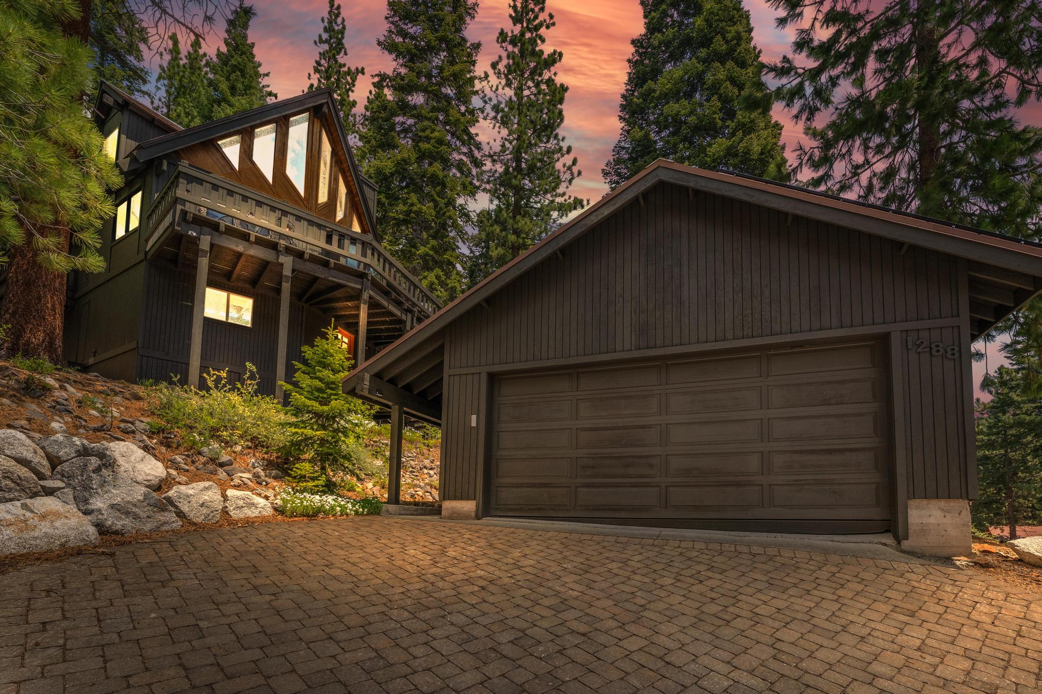 Large cabin-style vacation rental in Tahoe Vista, surrounded by pine trees, with a brick driveway and wooden facade at sunset.