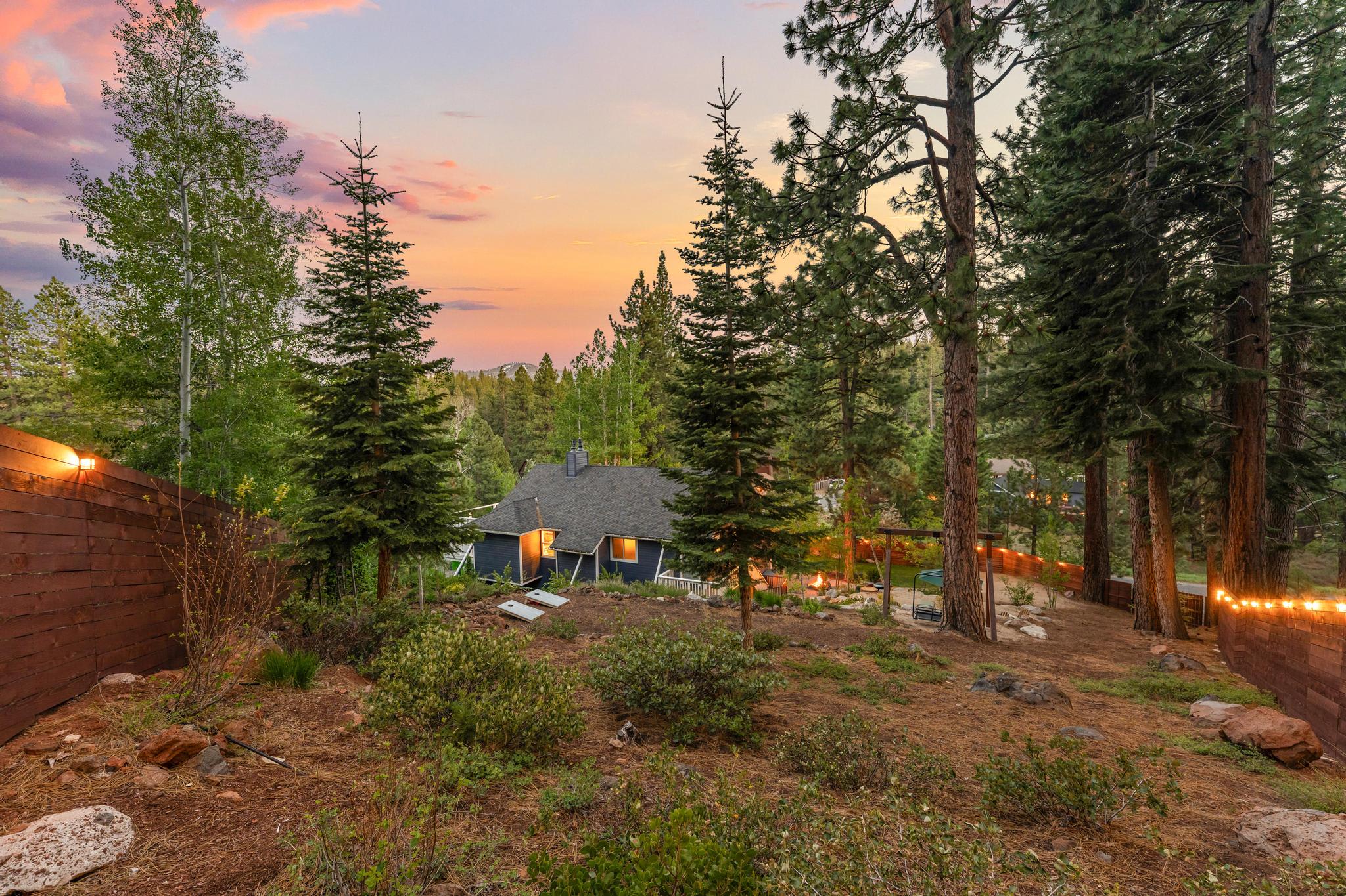Scenic view of a cozy vacation rental in Truckee, surrounded by tall pine trees and a colorful sunset sky.