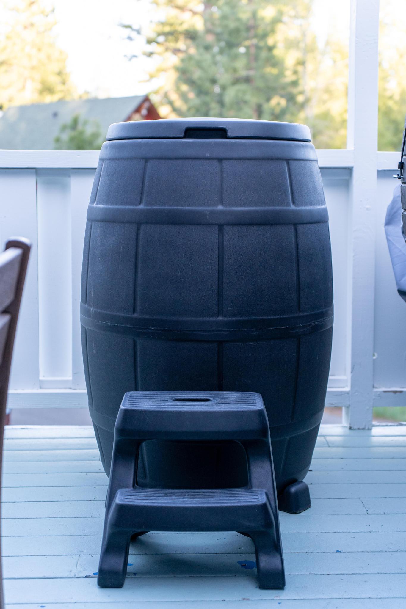 Black rain barrel with a step stool on a porch at a Truckee vacation rental, with trees in the background.