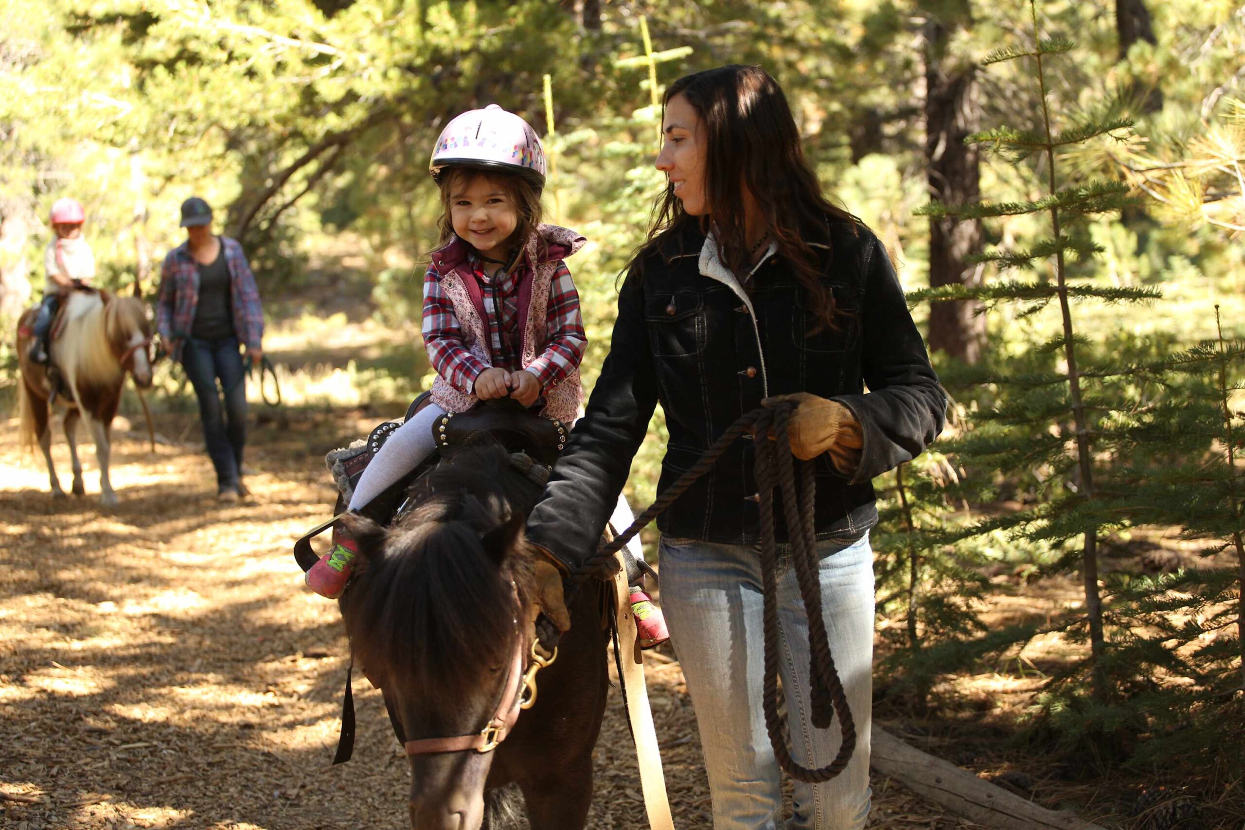 Child on horseback with an adult guide through woods near Truckee, promoting outdoor fun at a vacation rental.