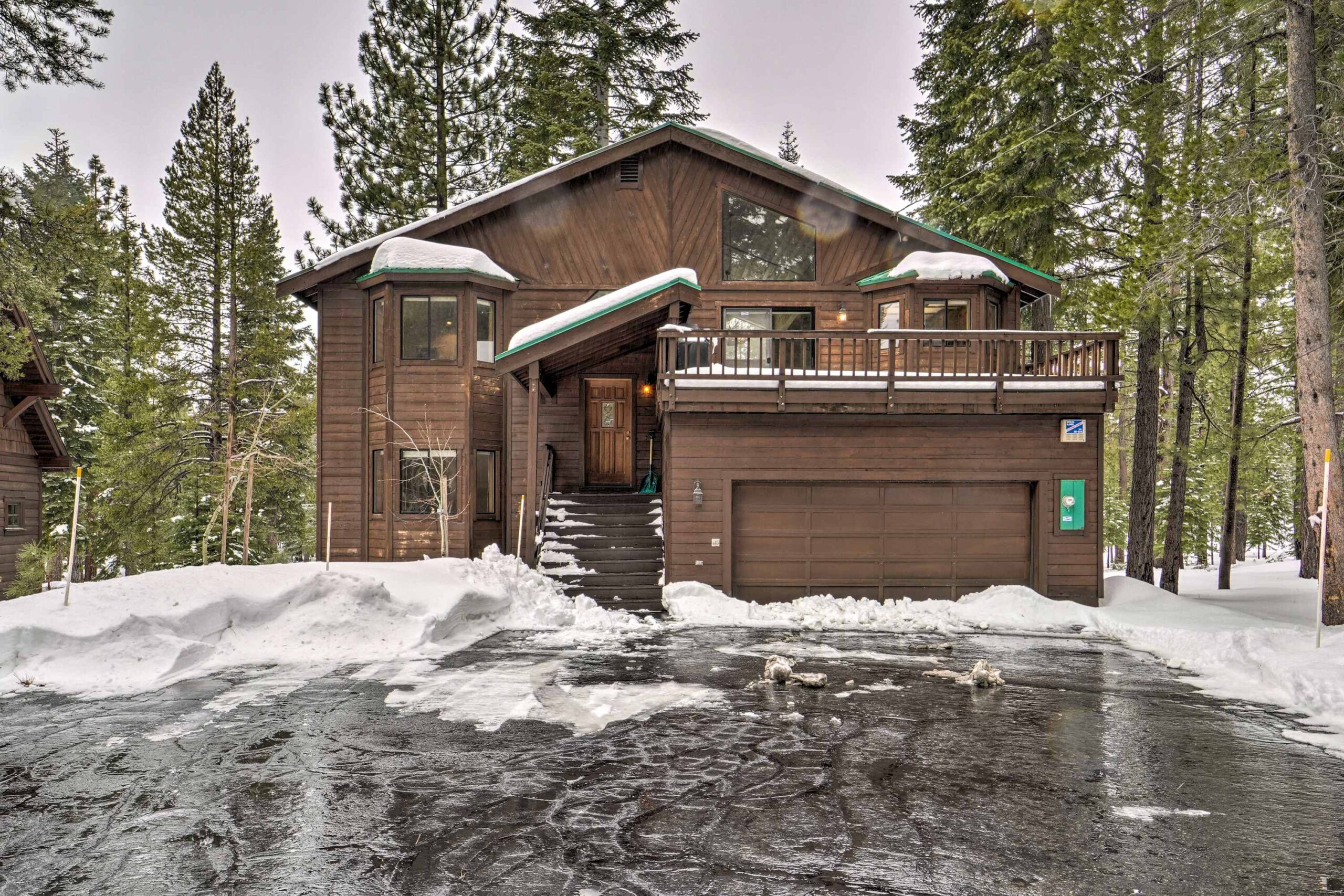 Cozy wooden vacation rental in snowy Truckee, surrounded by tall pine trees, with a spacious driveway and balcony.