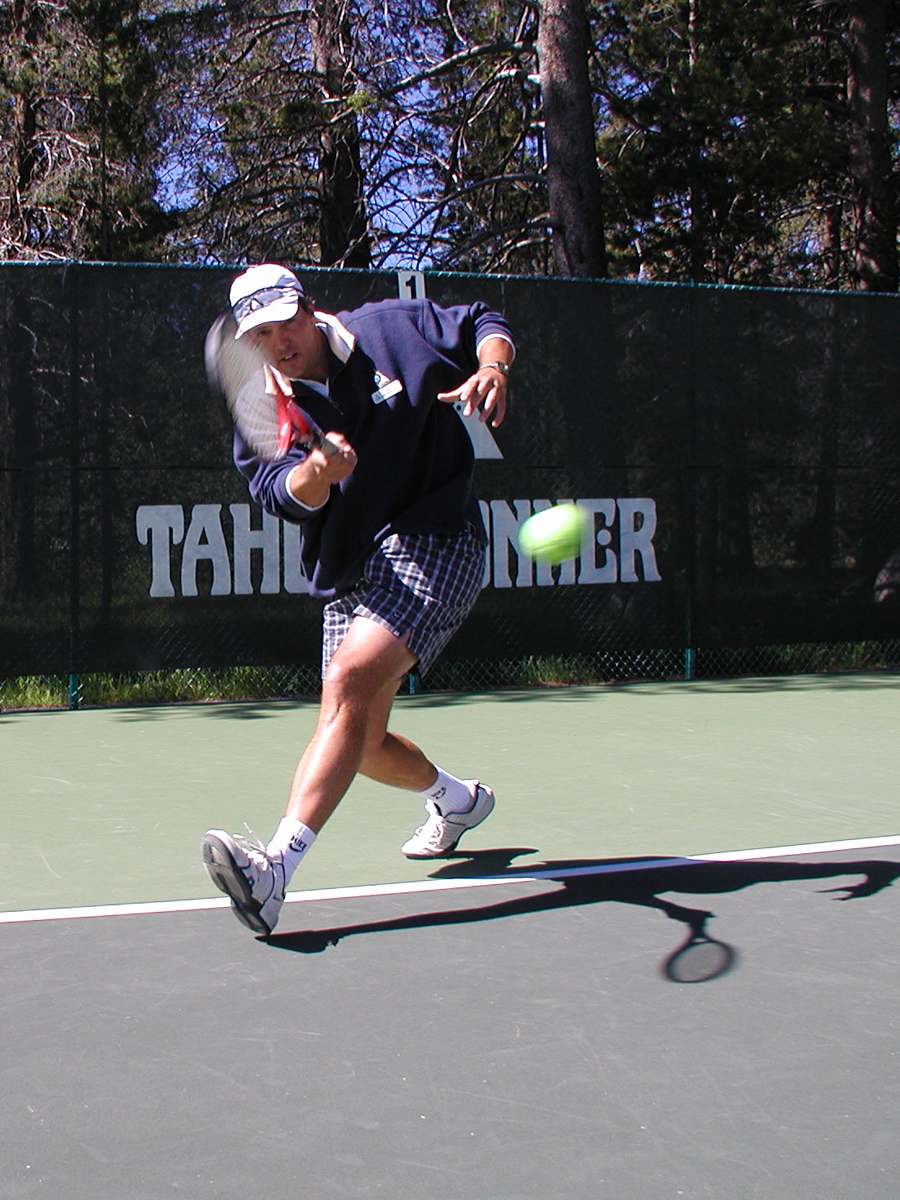 Tennis player hits a ball on a sunlit court in Truckee, showcasing amenities at a nearby vacation rental.