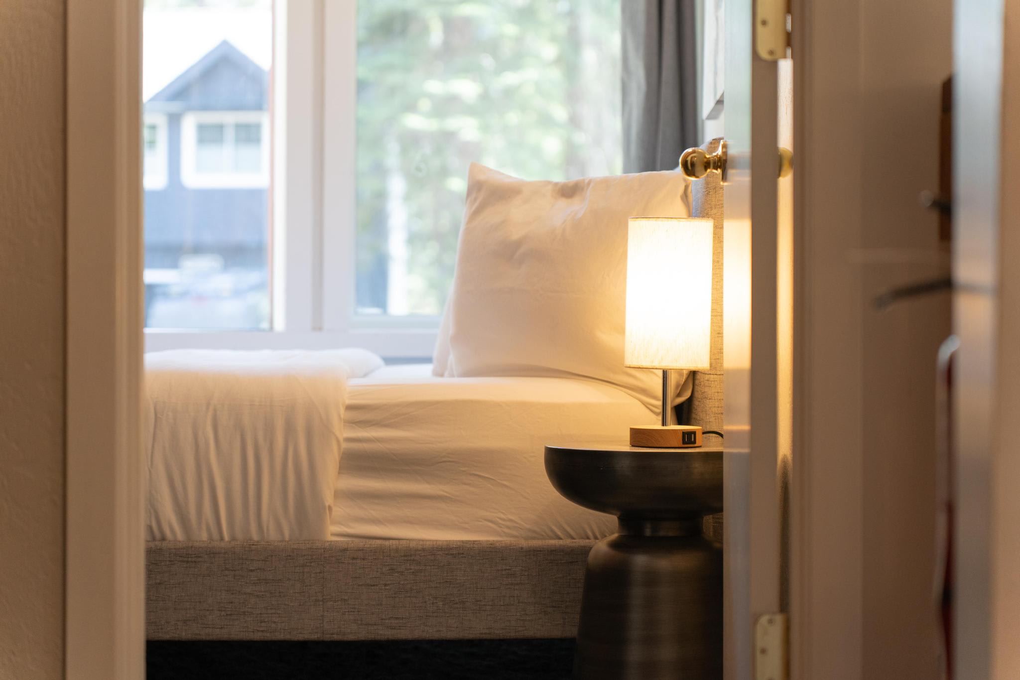 Cozy bedroom in a Tahoe Vista vacation rental featuring a soft bed, warm lighting, and a large window view.