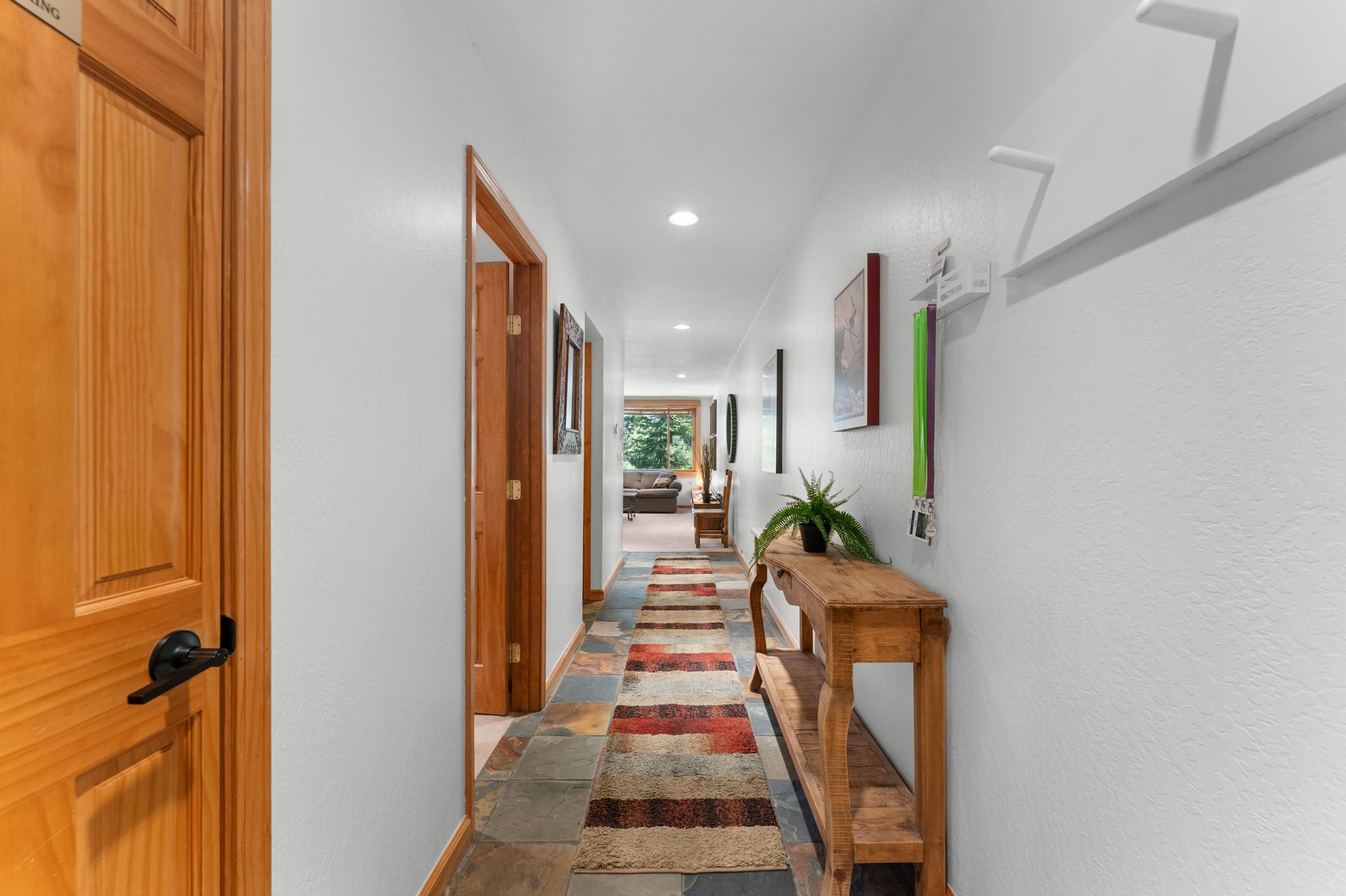 Hallway in a Truckee vacation rental, featuring a colorful runner, wooden door, artwork, and a view into a cozy living space.