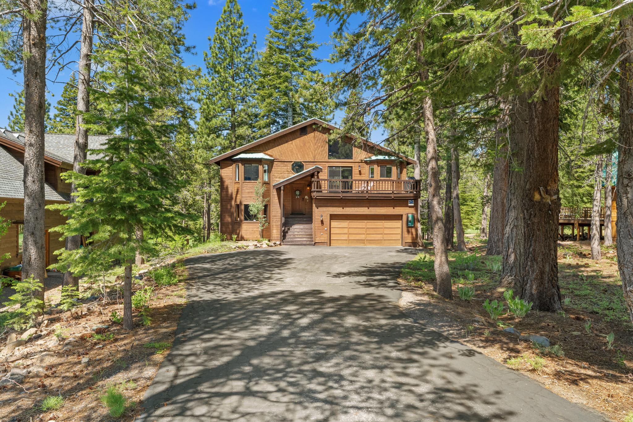 Wooden vacation rental in a forested area of Truckee, with a large driveway and surrounded by tall trees.