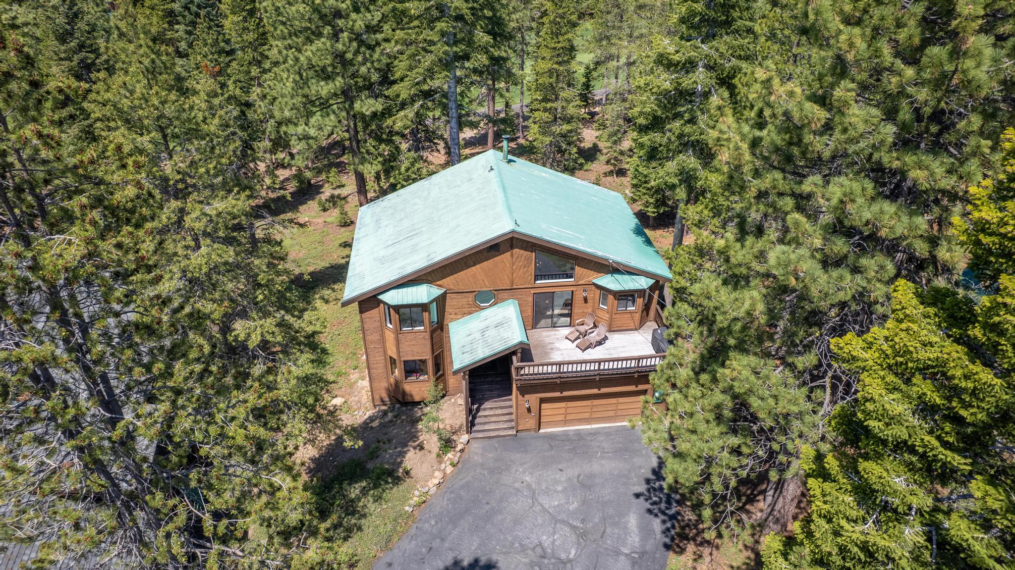 Aerial view of a rustic cabin vacation rental surrounded by trees in Truckee, featuring a green roof and deck.