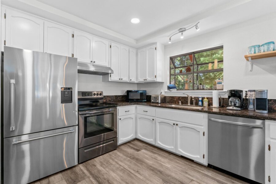Modern kitchen in Tahoe Vista vacation rental, featuring stainless steel appliances, white cabinets, and a window view.