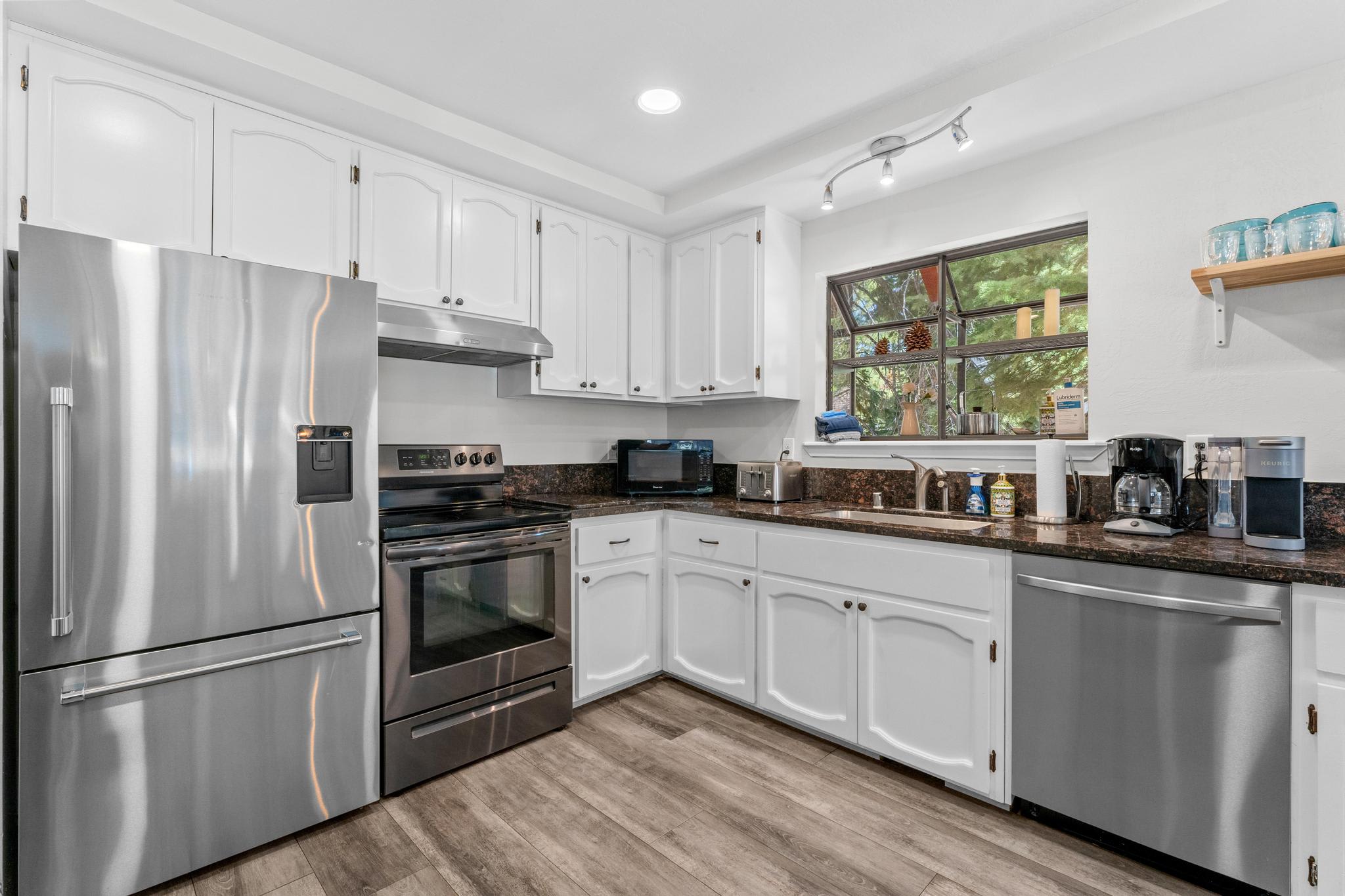 Modern kitchen in Tahoe Vista vacation rental, featuring stainless steel appliances, white cabinets, and a window view.
