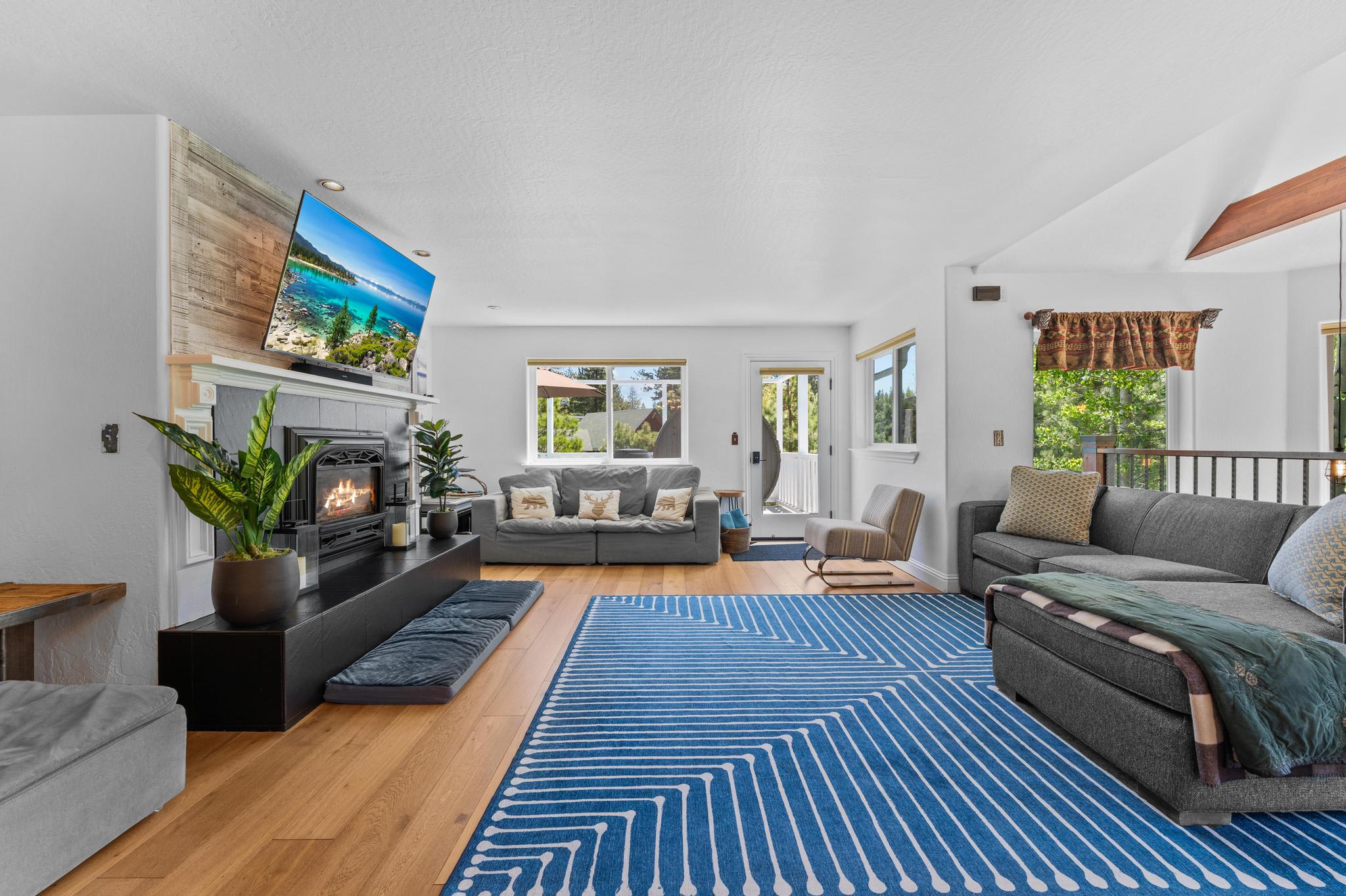 Spacious living room in Truckee vacation rental with cozy fireplace, modern decor, and large windows overlooking greenery.