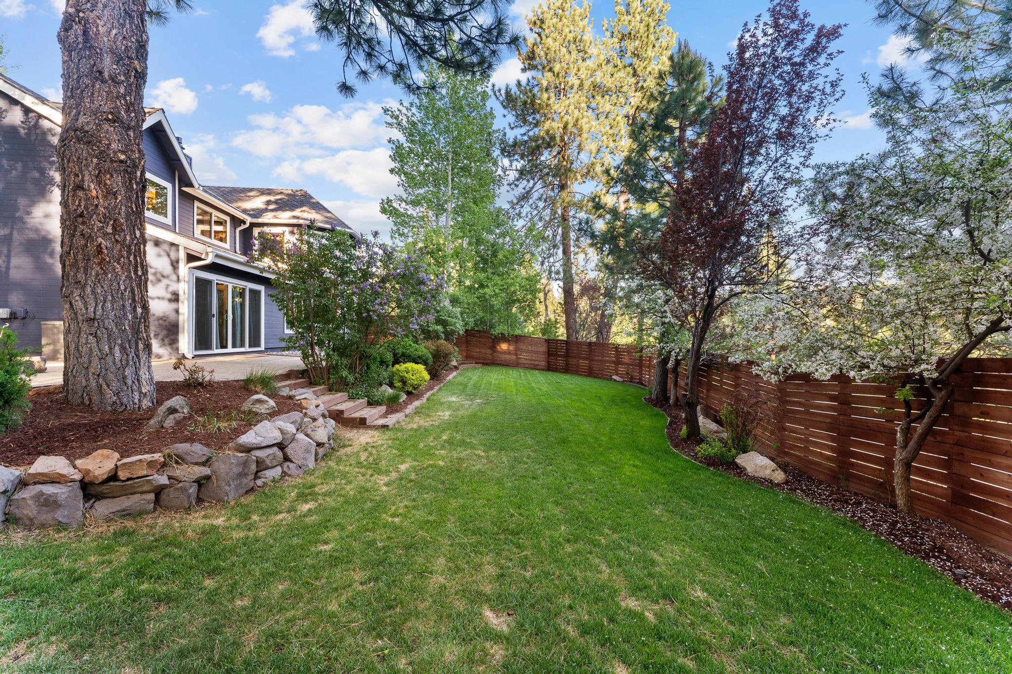 Backyard of a Truckee vacation rental with lush grass, stone-bordered garden, and wooden fence under a blue sky.