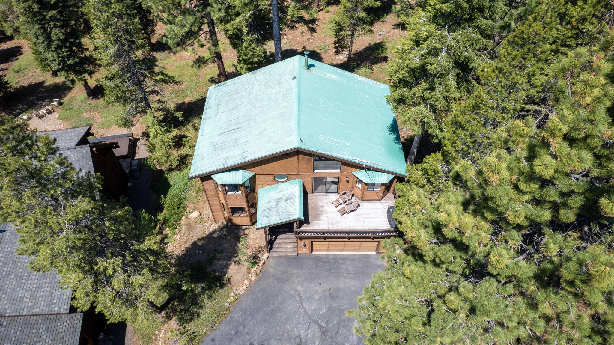 Aerial view of a rustic vacation rental in Truckee, surrounded by lush greenery and tall trees.