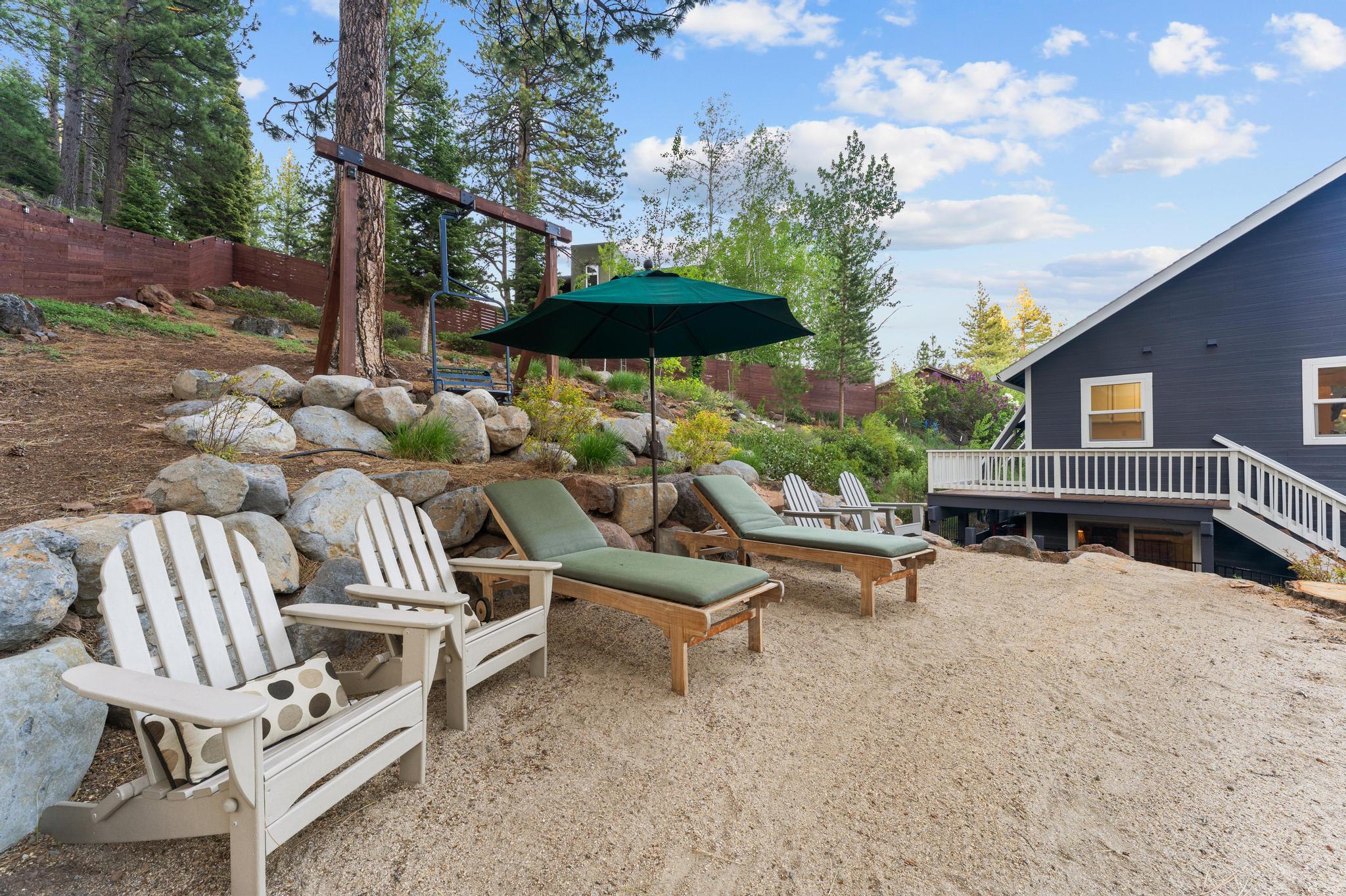 Outdoor seating area at a Truckee vacation rental with lounge chairs and parasol, surrounded by trees and rocks.