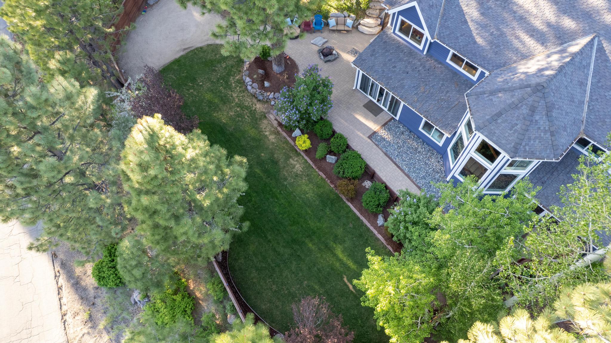 Aerial view of a charming vacation rental in Truckee, featuring a well-manicured lawn and surrounding pine trees.