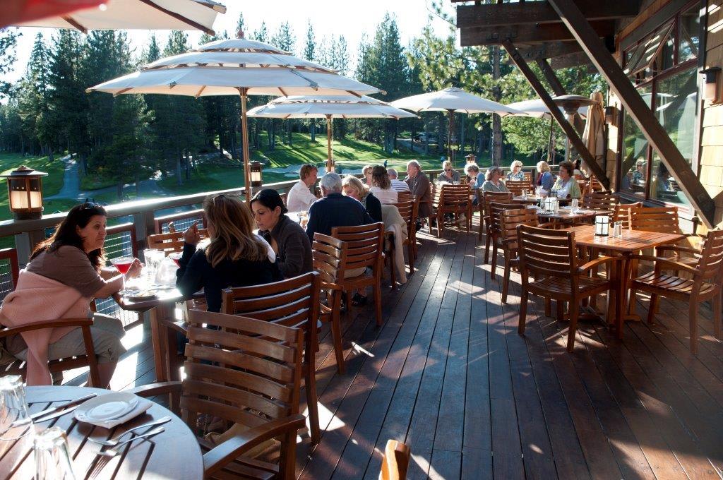 Outdoor dining area at a Truckee vacation rental, with people enjoying drinks under white umbrellas amid pine trees.
