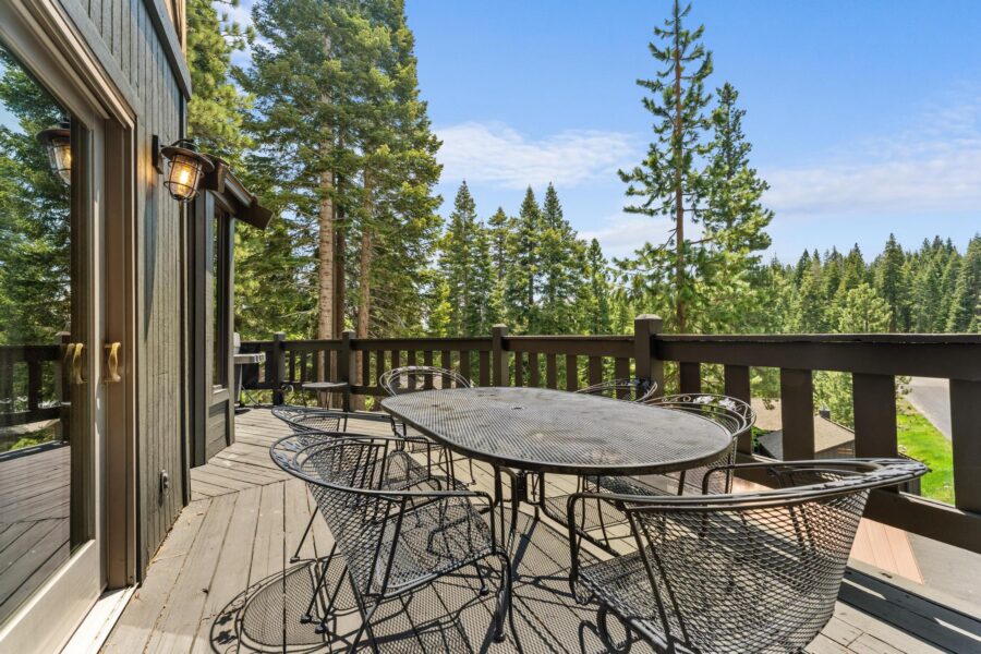 Deck of a Tahoe Vista vacation rental with metal furniture, overlooking tall pine trees under a blue sky.