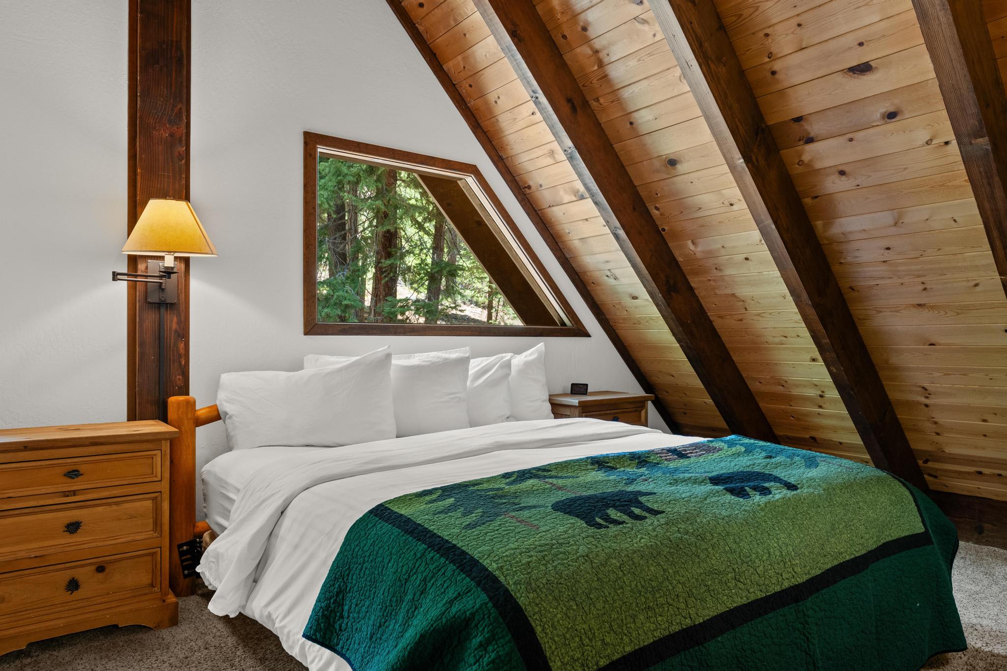 Cozy A-frame bedroom in Tahoe Vista vacation rental, featuring wooden walls, triangular window, and forest quilt.