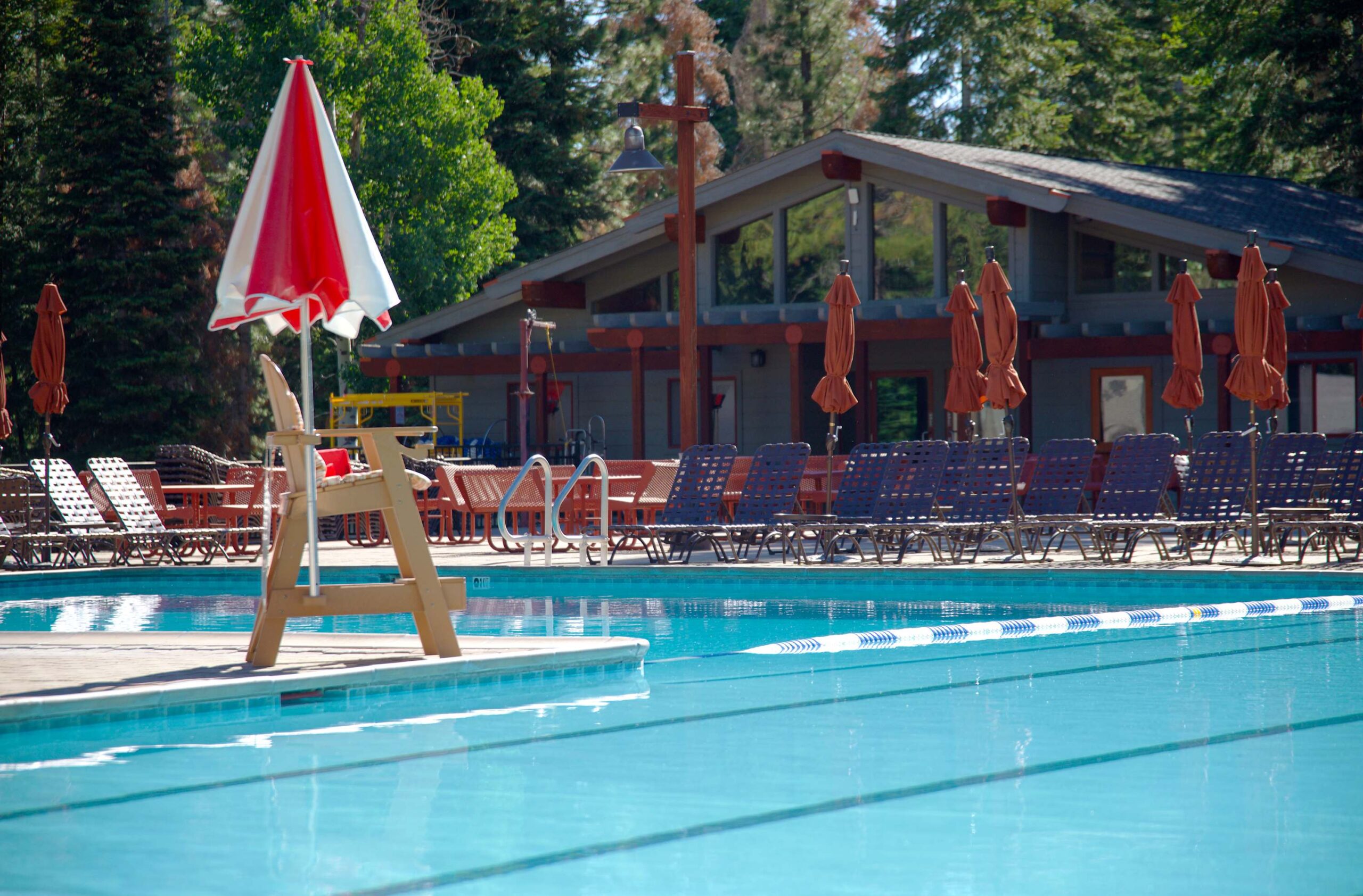 Outdoor pool at a Truckee vacation rental, surrounded by lounge chairs and a red umbrella, with a lodge in the background.