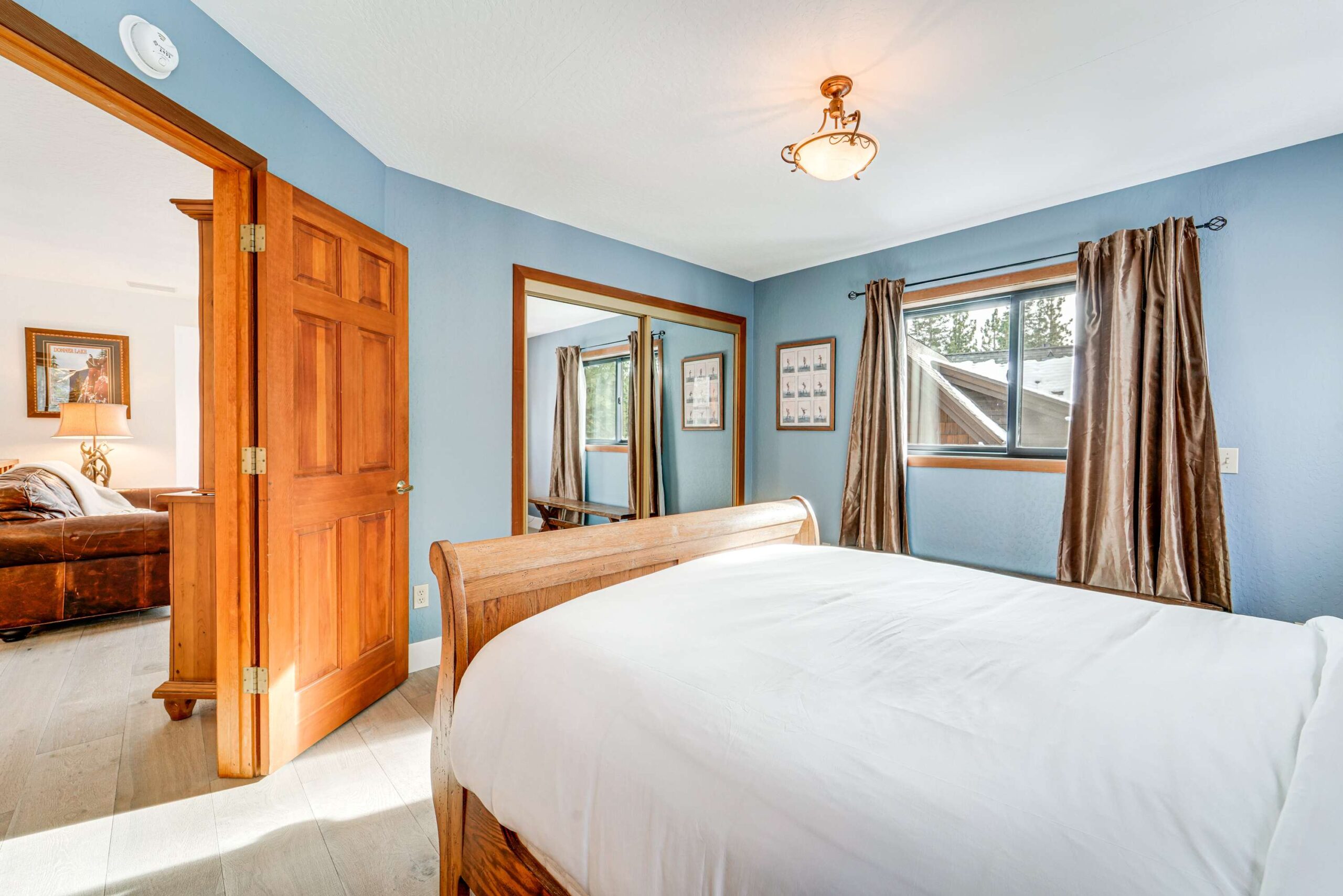 Cozy bedroom in Truckee vacation rental with wood accents, mirrored closet, and large window.