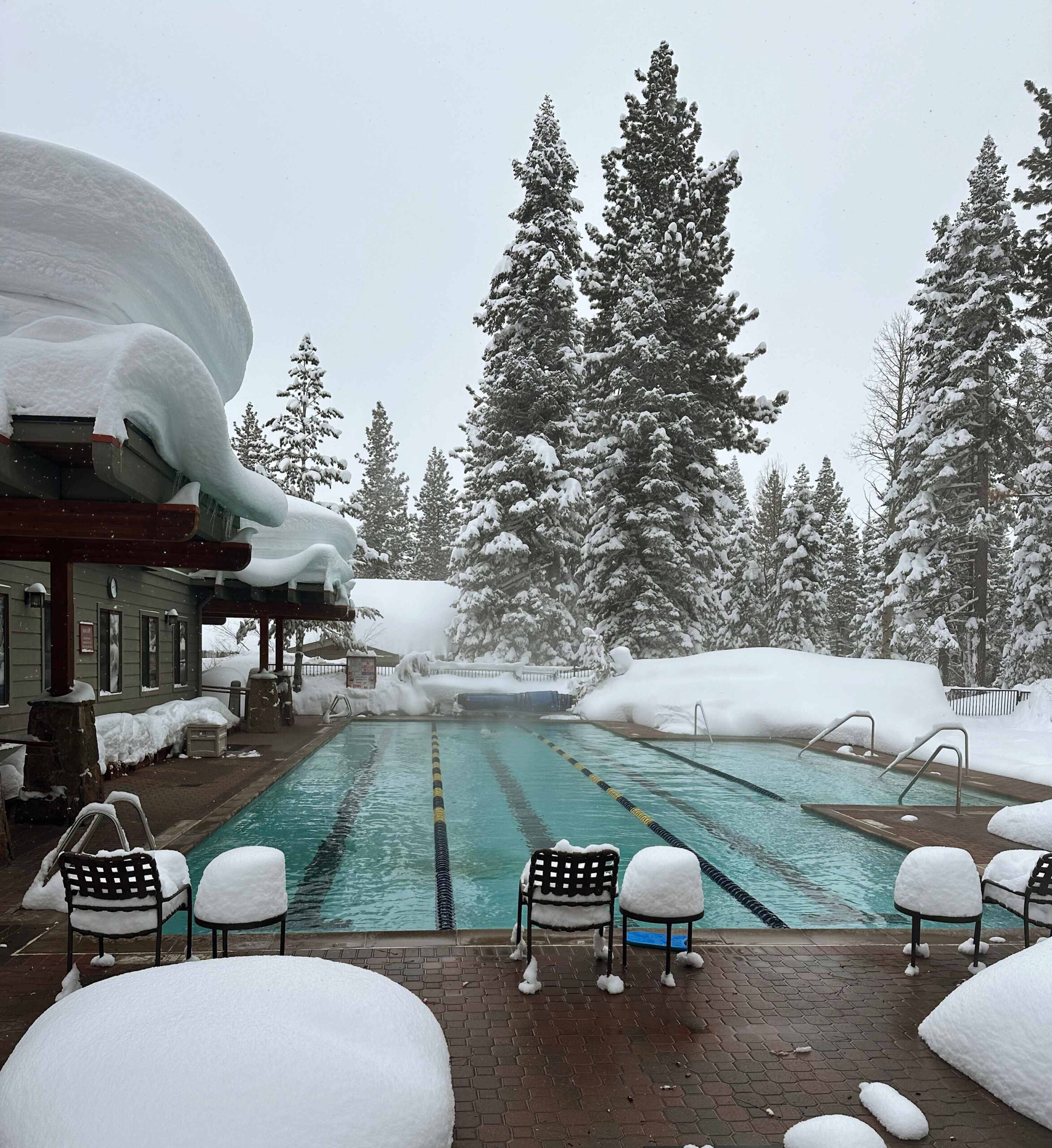 Snowy poolside at a Truckee vacation rental, surrounded by snow-covered trees and a cozy building.