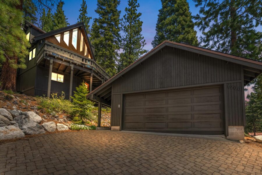 Charming A-frame vacation rental in Tahoe Vista, surrounded by tall pine trees with a stone driveway and cozy ambiance.