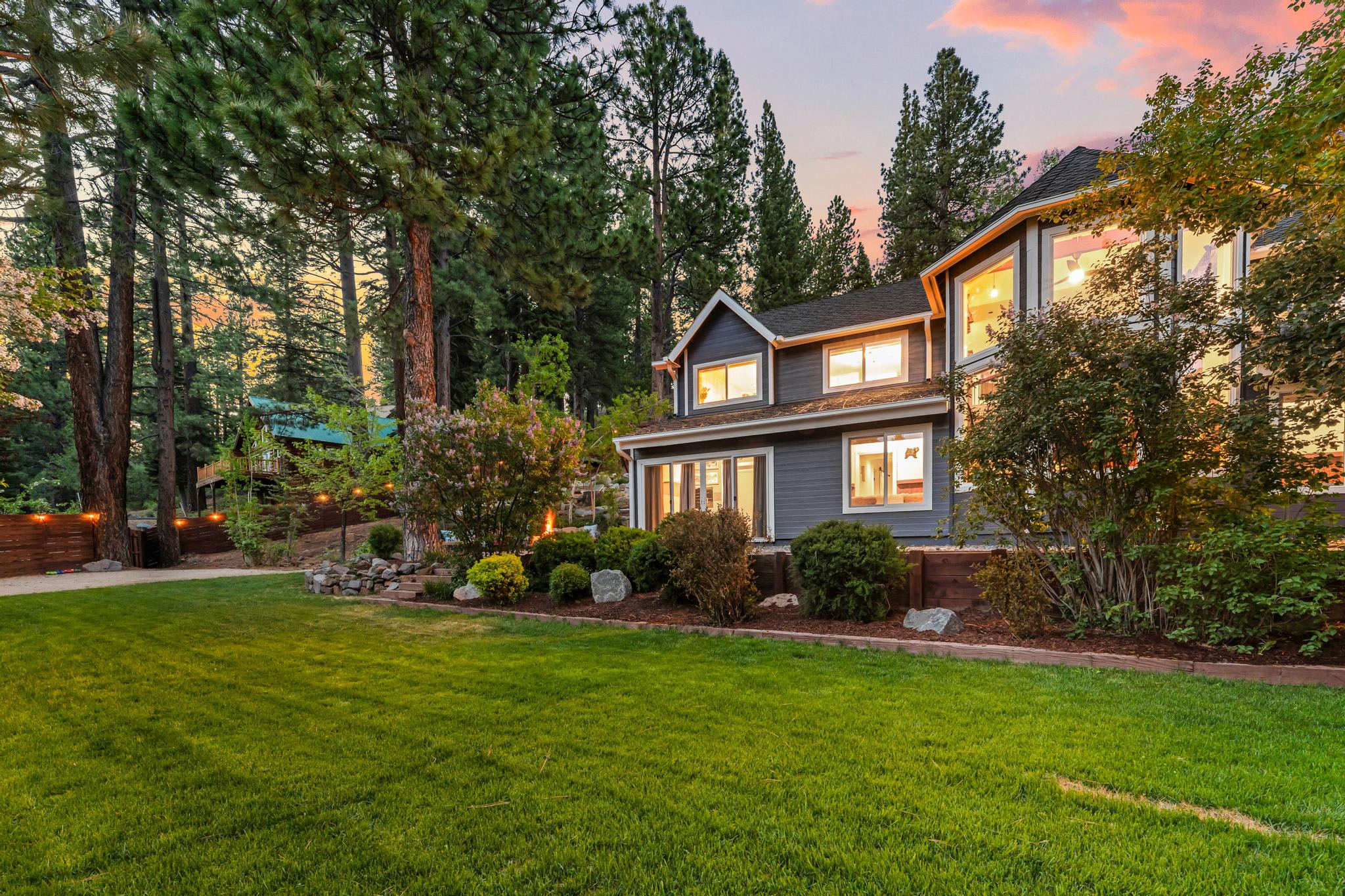 Cozy vacation rental in Truckee surrounded by lush trees and a well-manicured lawn, with a warm glowing sunset sky.