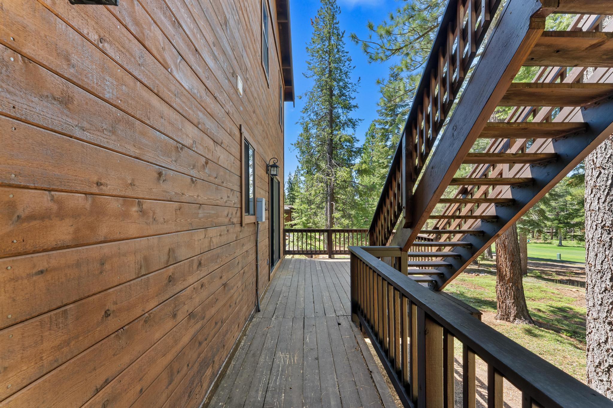 Wooden deck and stairs of a vacation rental in Truckee, surrounded by tall pine trees under a clear blue sky.
