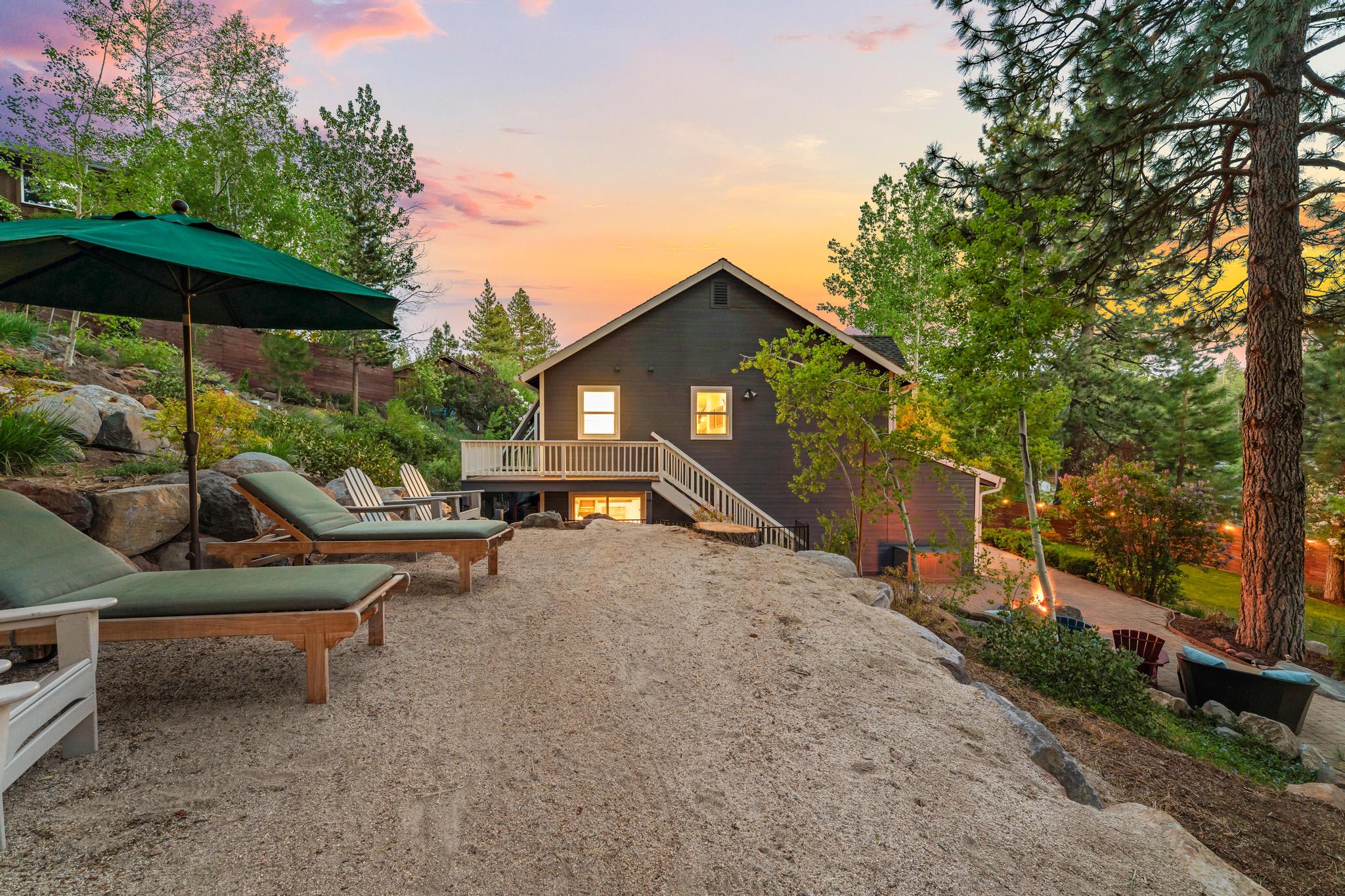Vacation rental in Truckee at sunset. Cozy backyard with lounge chairs, umbrella, and trees surrounding the house.