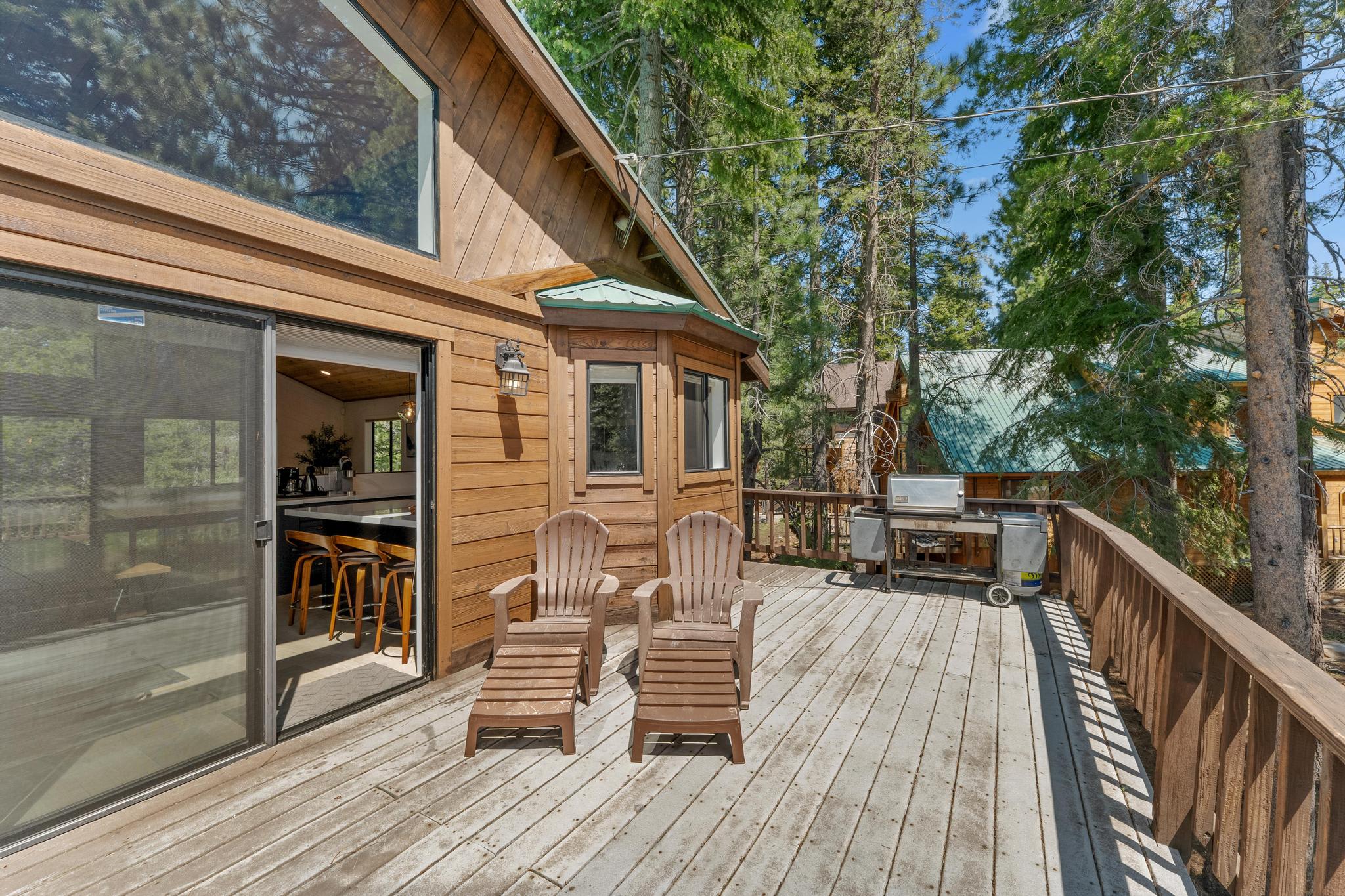 Spacious wooden deck at a Truckee vacation rental with seating and a grill, surrounded by lush trees.