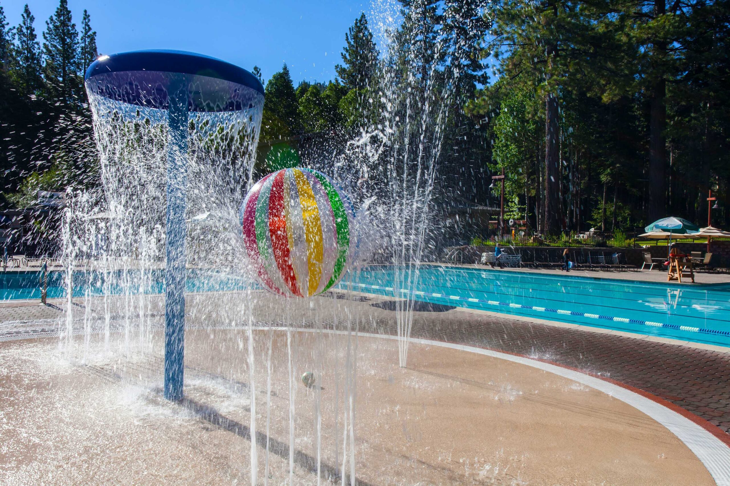 Colorful water play area at a vacation rental in Truckee, featuring a splash pad and pool surrounded by trees.
