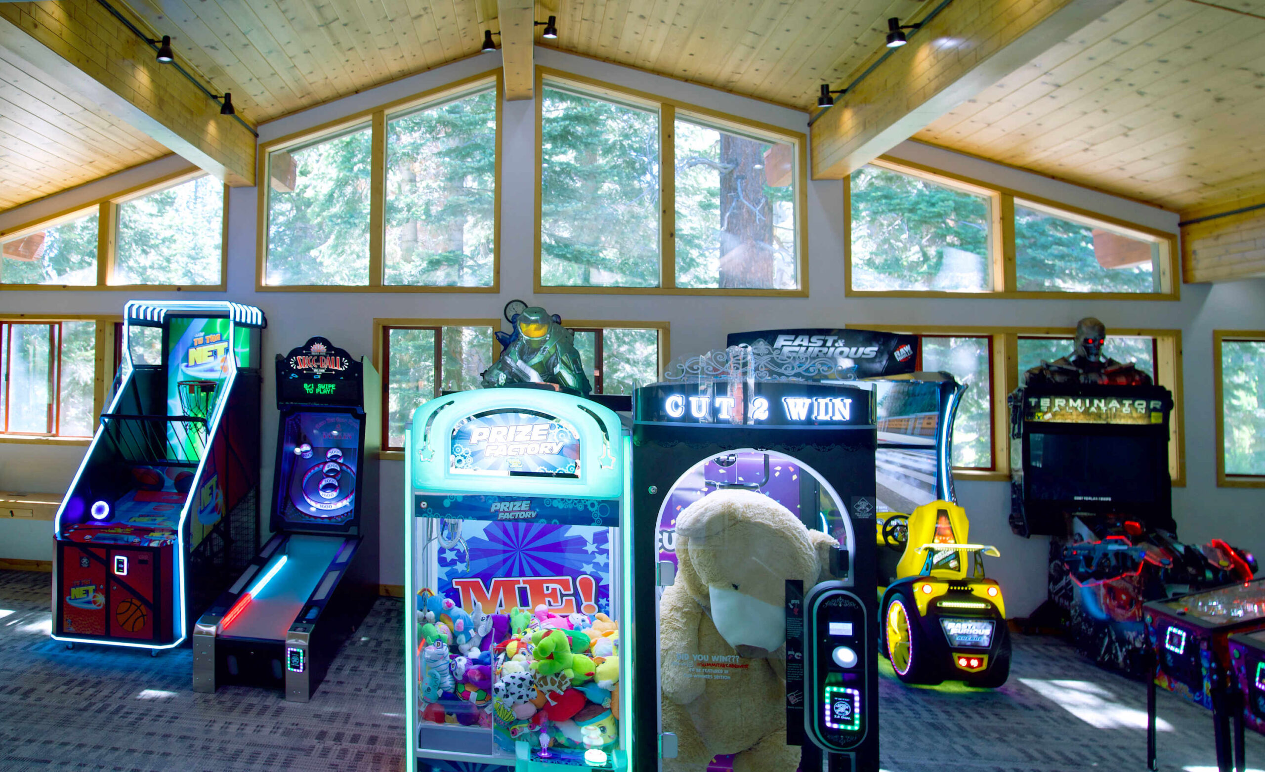 Arcade room in a Truckee vacation rental with various gaming machines and large windows overlooking trees.