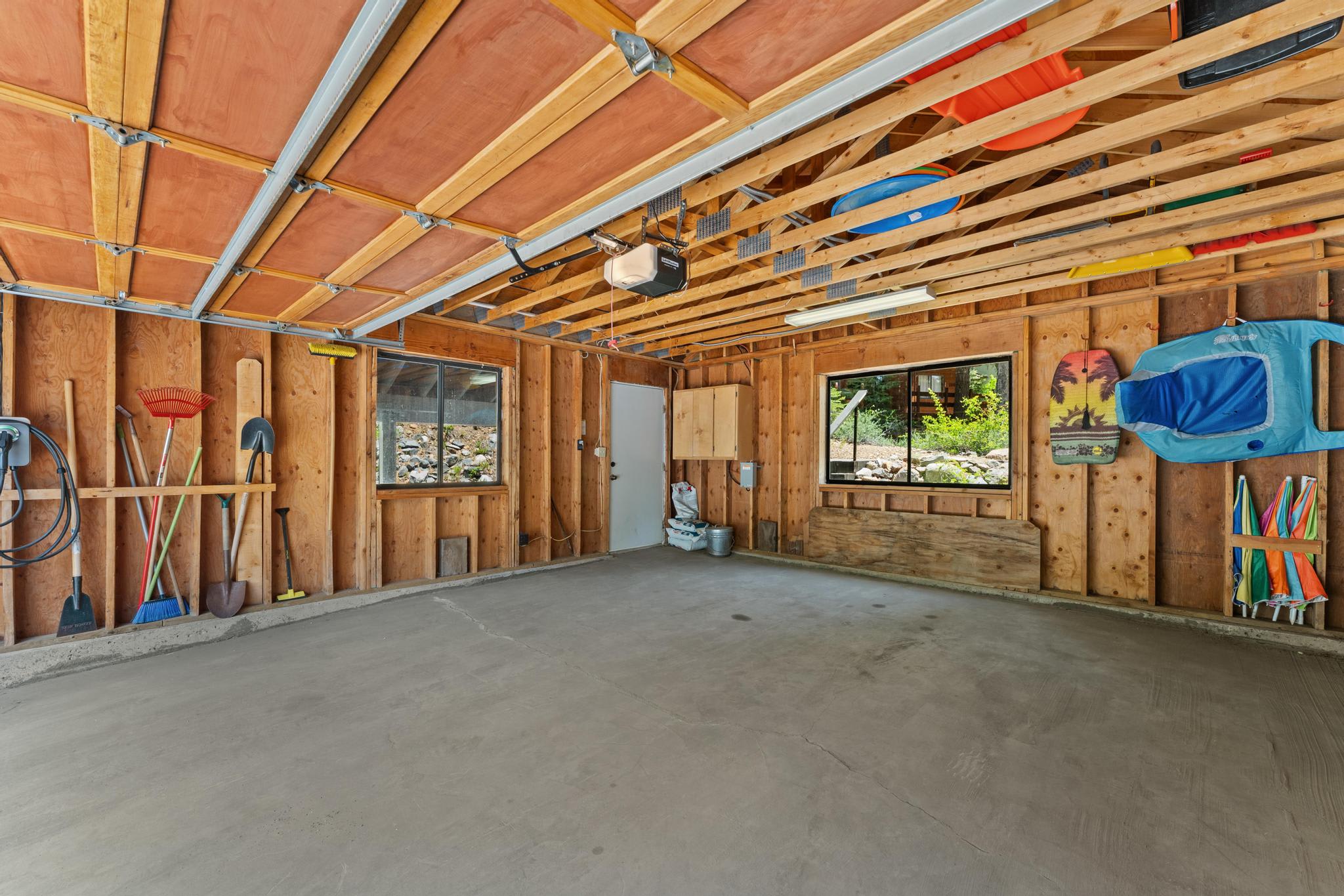 Garage in a Tahoe Vista vacation rental with wooden beams, tools, and windows overlooking greenery.