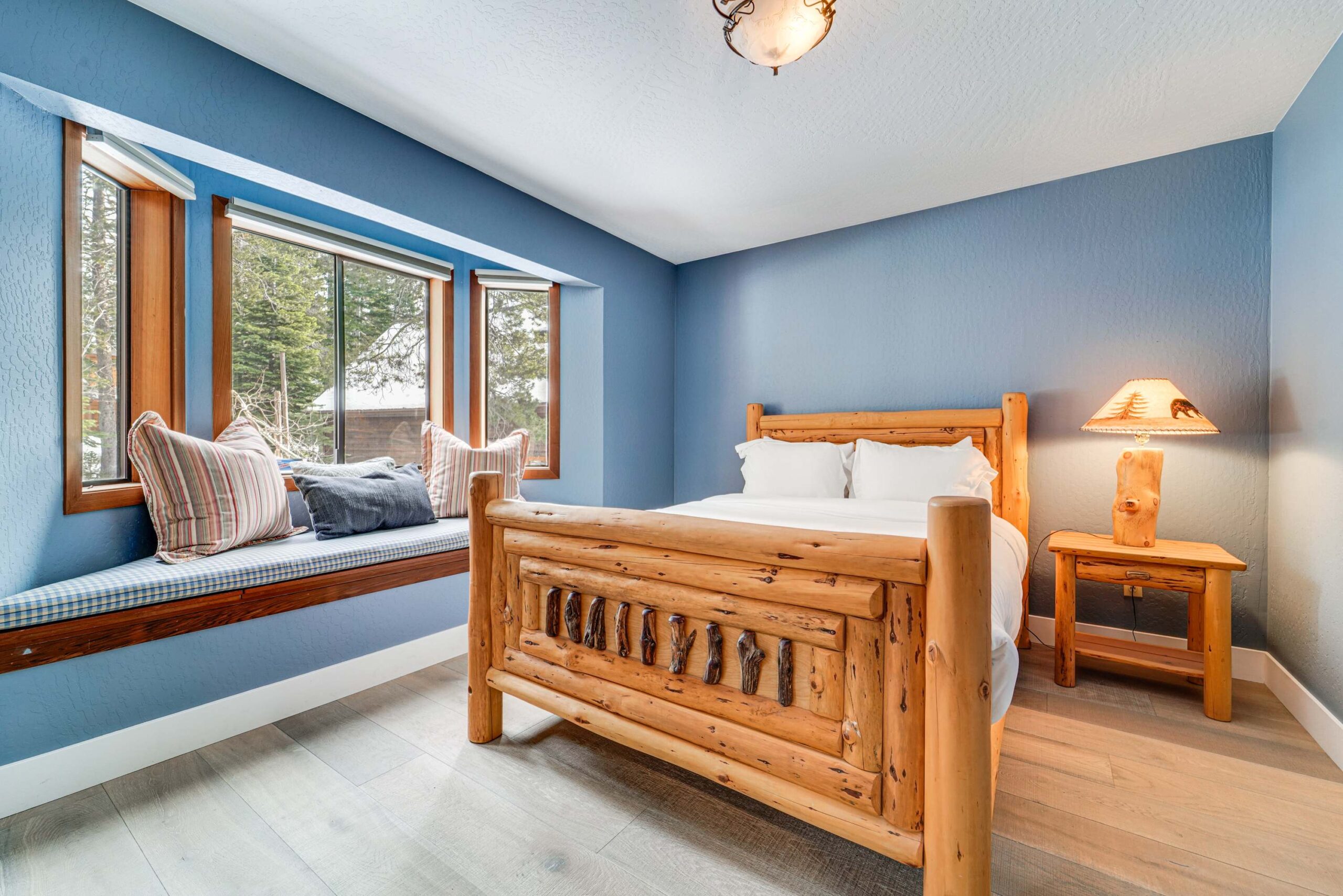 Rustic bedroom in a Truckee vacation rental with log bed, blue walls, bay window seat, and wooden nightstand.