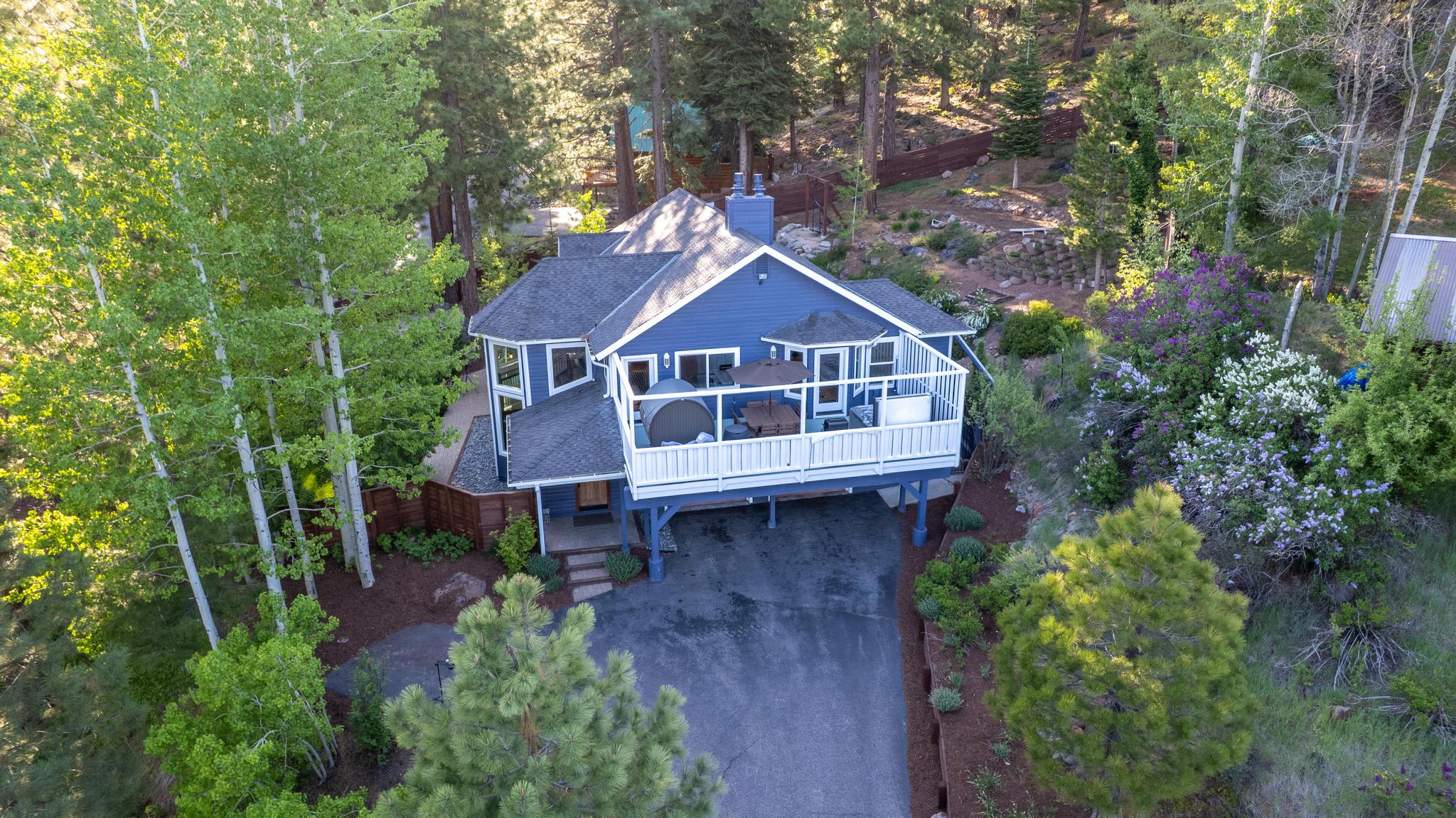 Aerial view of a charming blue vacation rental surrounded by trees in Truckee, featuring a spacious deck and lush garden.