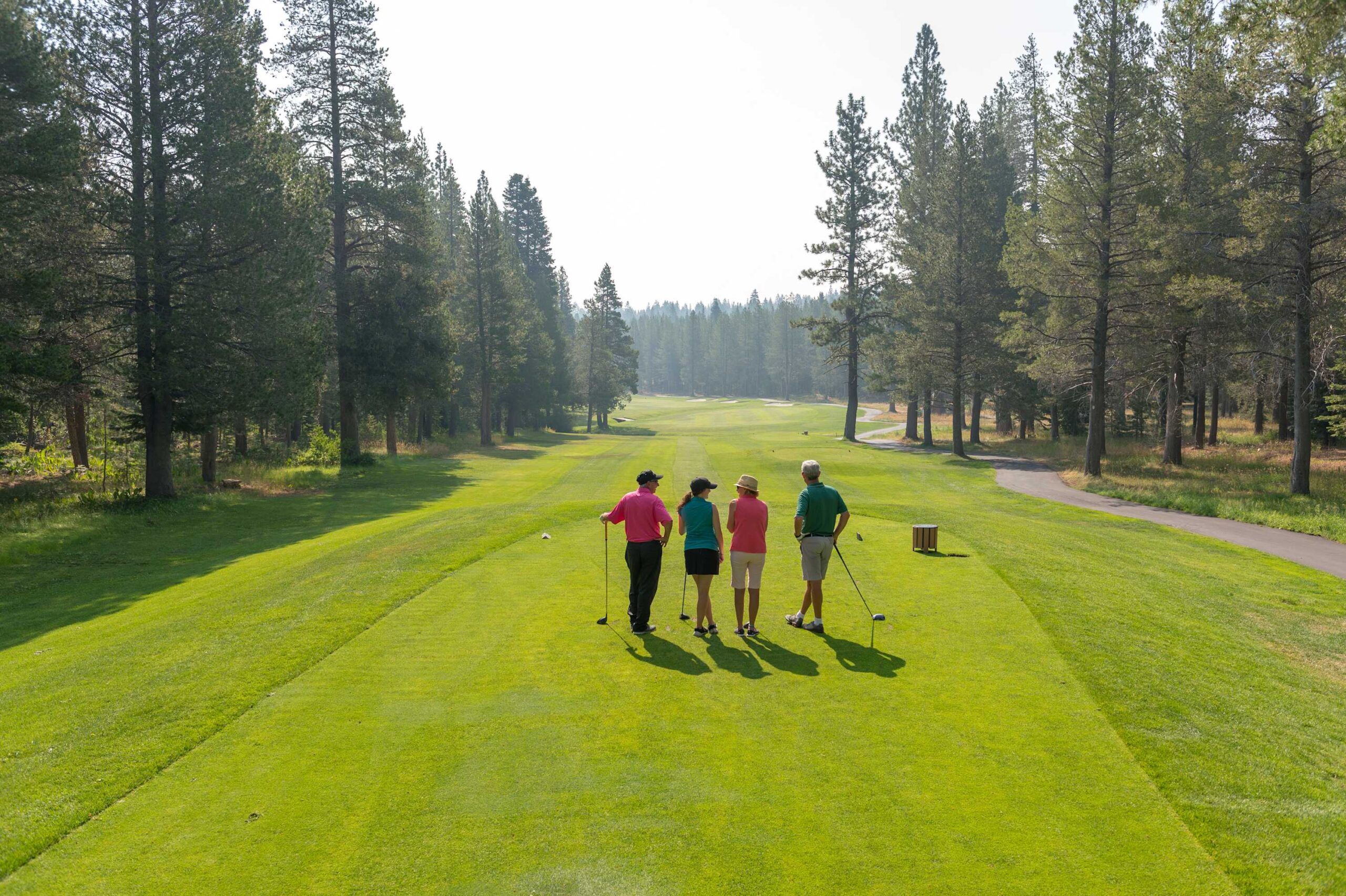 Four people golfing on a lush course in Truckee, surrounded by tall trees, perfect for a vacation rental experience.
