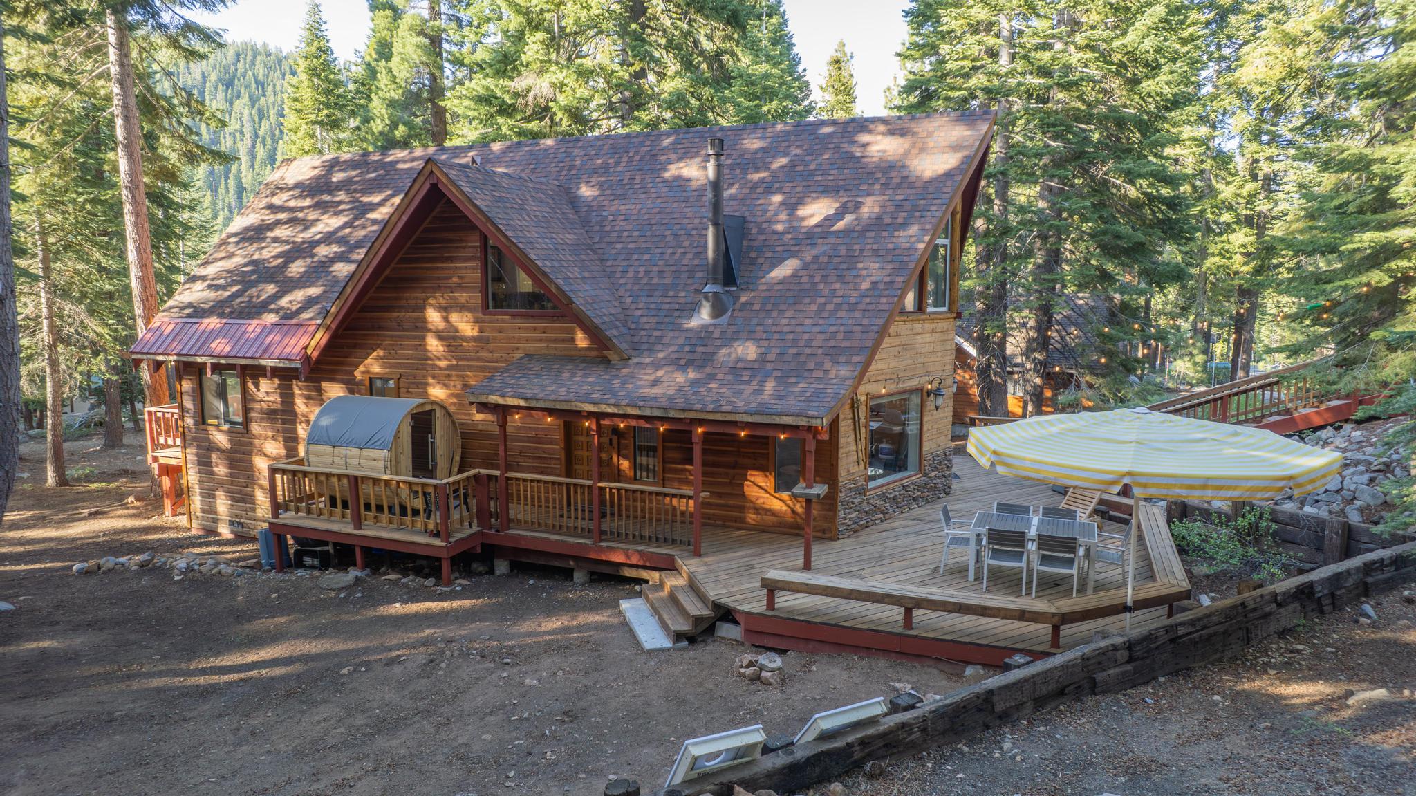 Rustic cabin vacation rental in Tahoe Vista, surrounded by pine trees, featuring a spacious deck and outdoor seating.