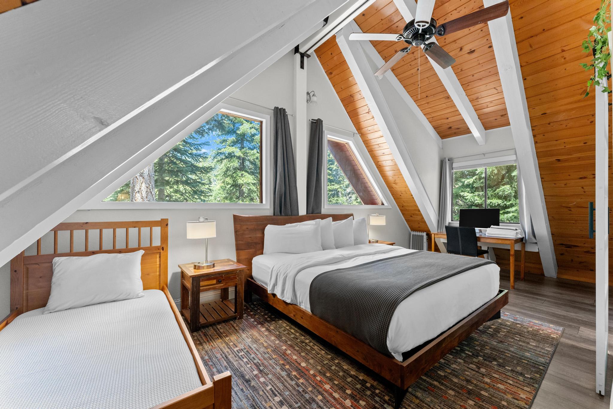 A-frame Tahoe Vista vacation rental bedroom with wood accents, large windows, twin and king beds, and a cozy desk area.