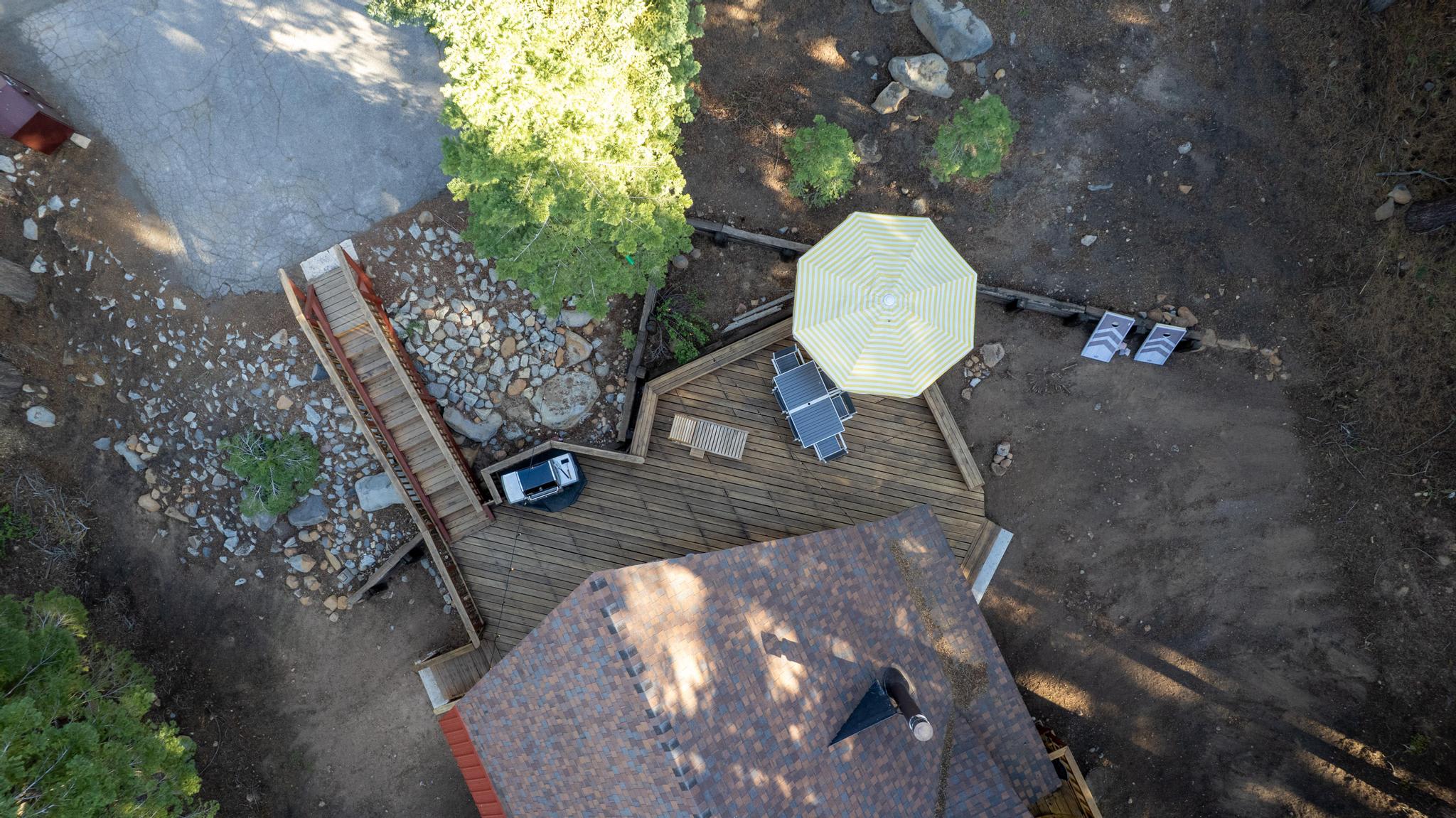 Aerial view of a Tahoe Vista vacation rental deck, surrounded by trees and rocks, with chairs and a large patio umbrella.