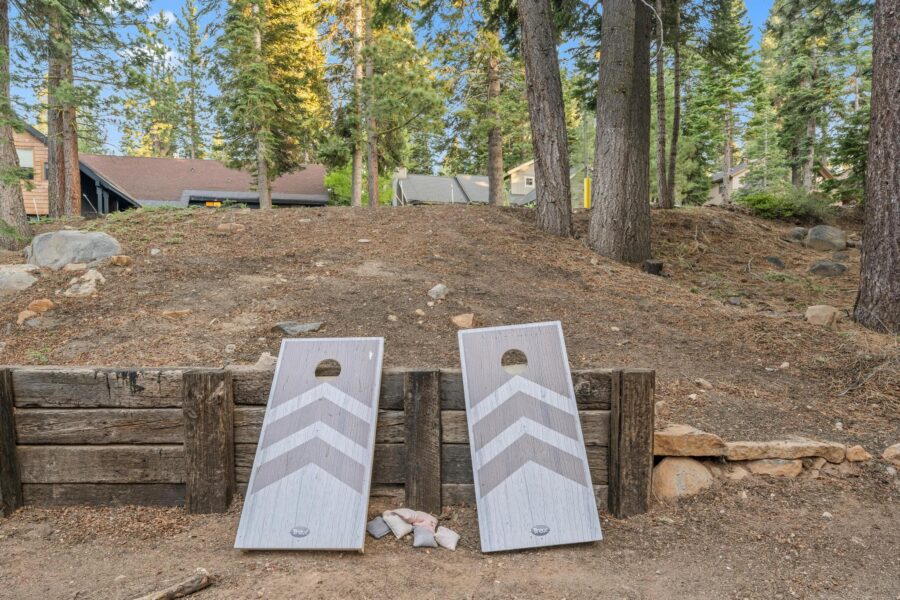 Cornhole boards in a forested yard at a Tahoe Vista vacation rental, surrounded by trees and cabins.