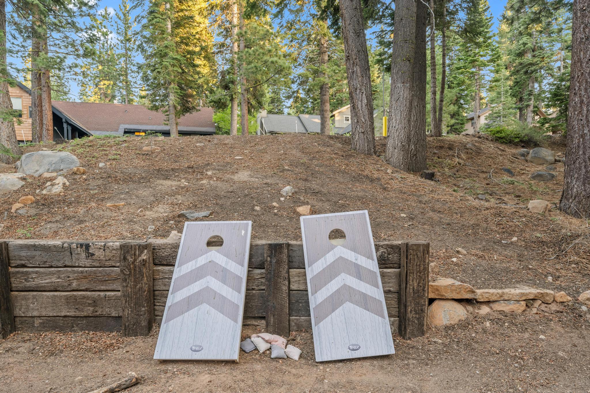 Cornhole boards in a forested yard at a Tahoe Vista vacation rental, surrounded by trees and cabins.
