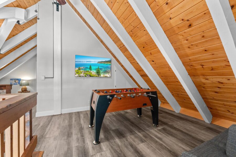 Loft area in Tahoe Vista vacation rental with foosball table, angled wood ceiling, and wall-mounted TV.